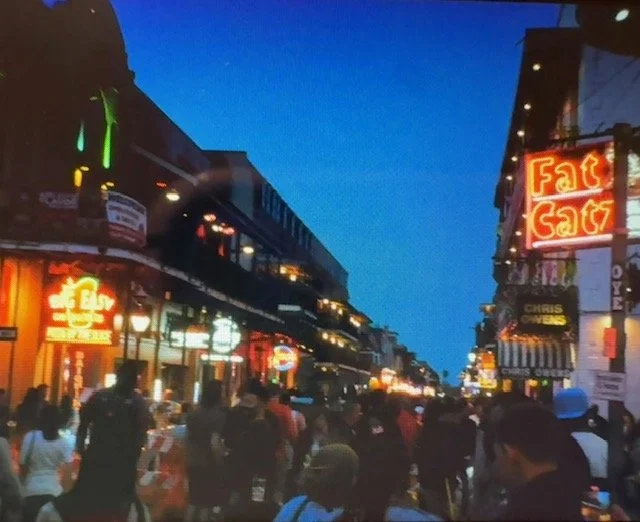 Bourbon Street lit up at night with neon signs and crowds filling the street.