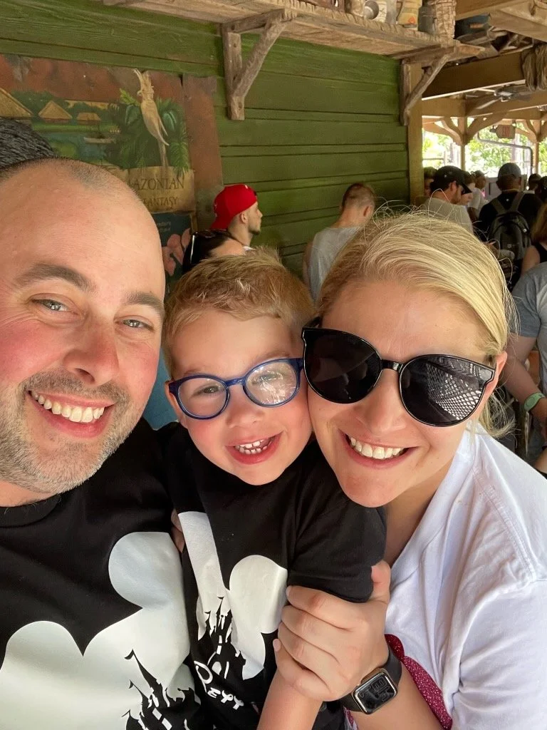 a mom dad and son posing for a picture in line for a ride