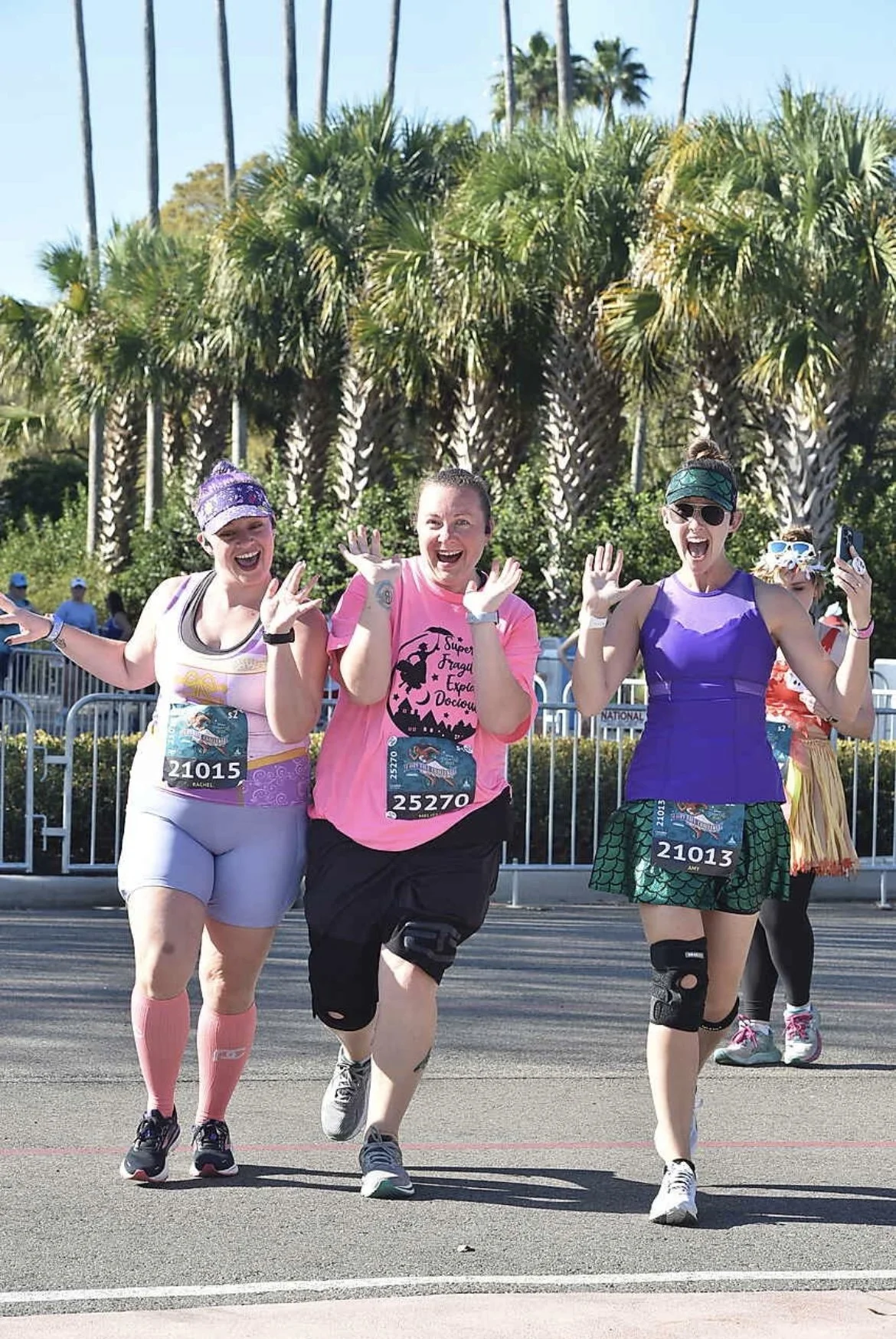 Three costumed runners cheer and pose together under palm trees during a Walt Disney World race weekend.