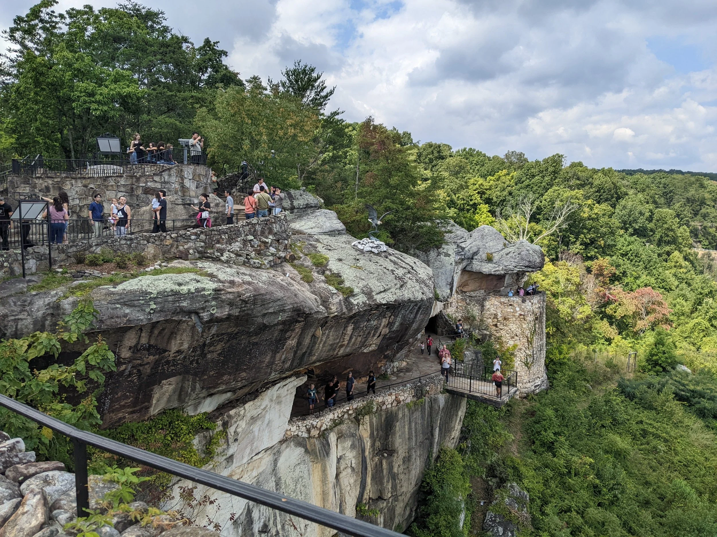 a rocky cliff with trees surrounding it and multiple walk ways with people walking along it