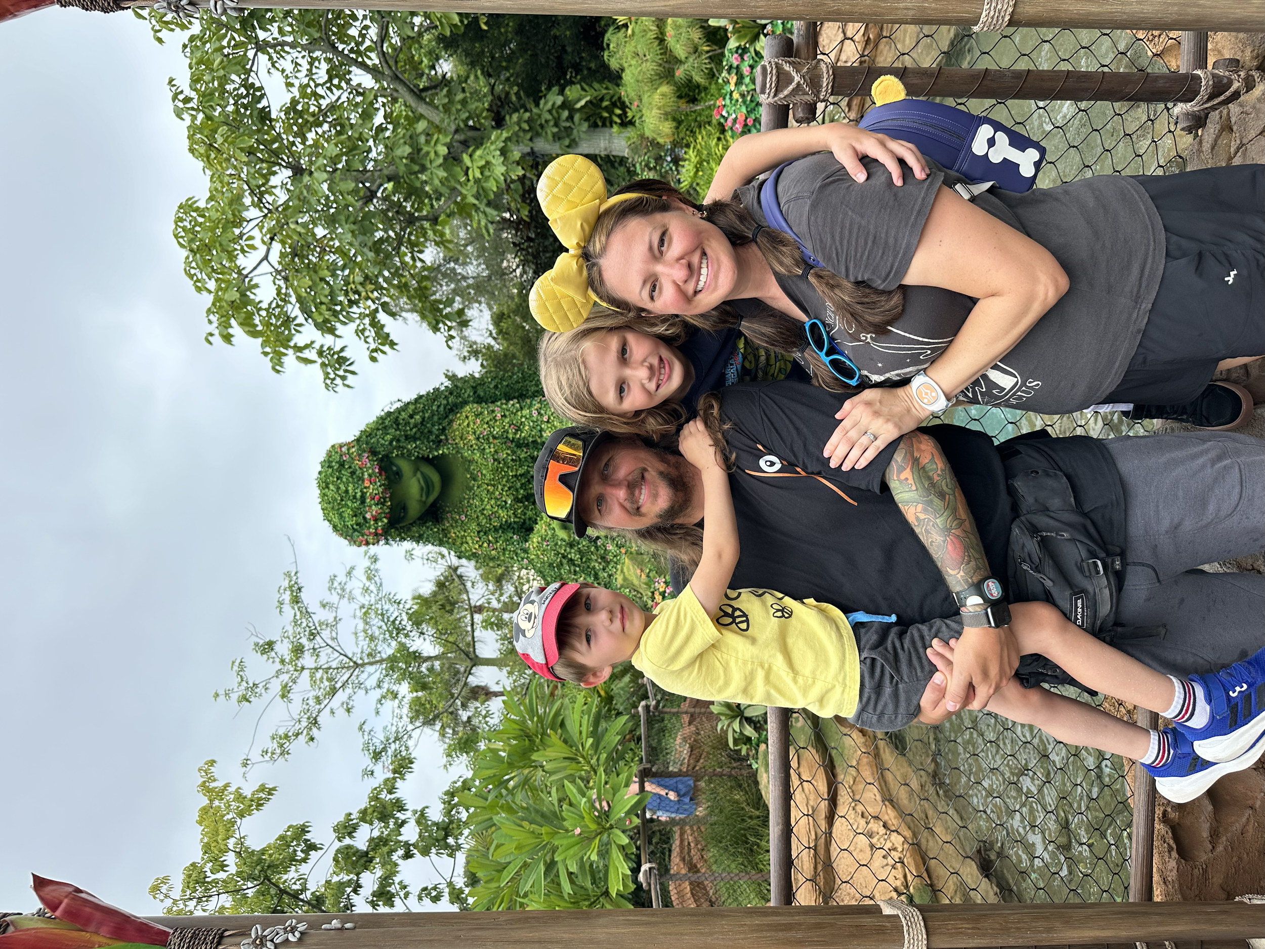 a family of 4 smiling in front of a moana topiaries