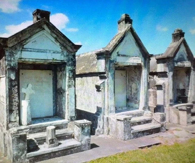 Historic above-ground tombs in a New Orleans cemetery, with ornate stone mausoleums under a blue sky.