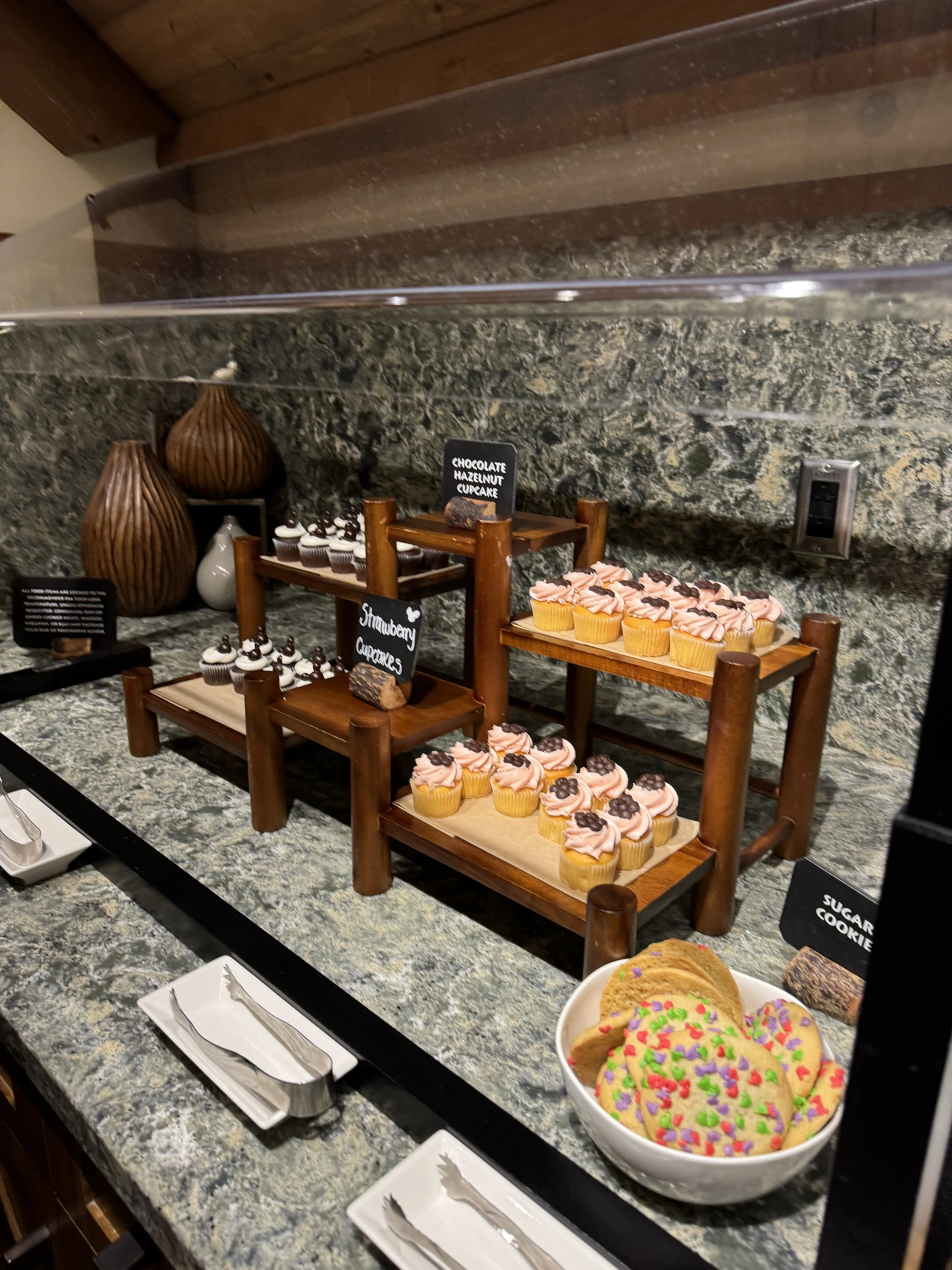 A dessert display of chocolate hazelnut cupcakes, strawberry cupcakes, and sugar cookies at a Disney Club Level lounge.