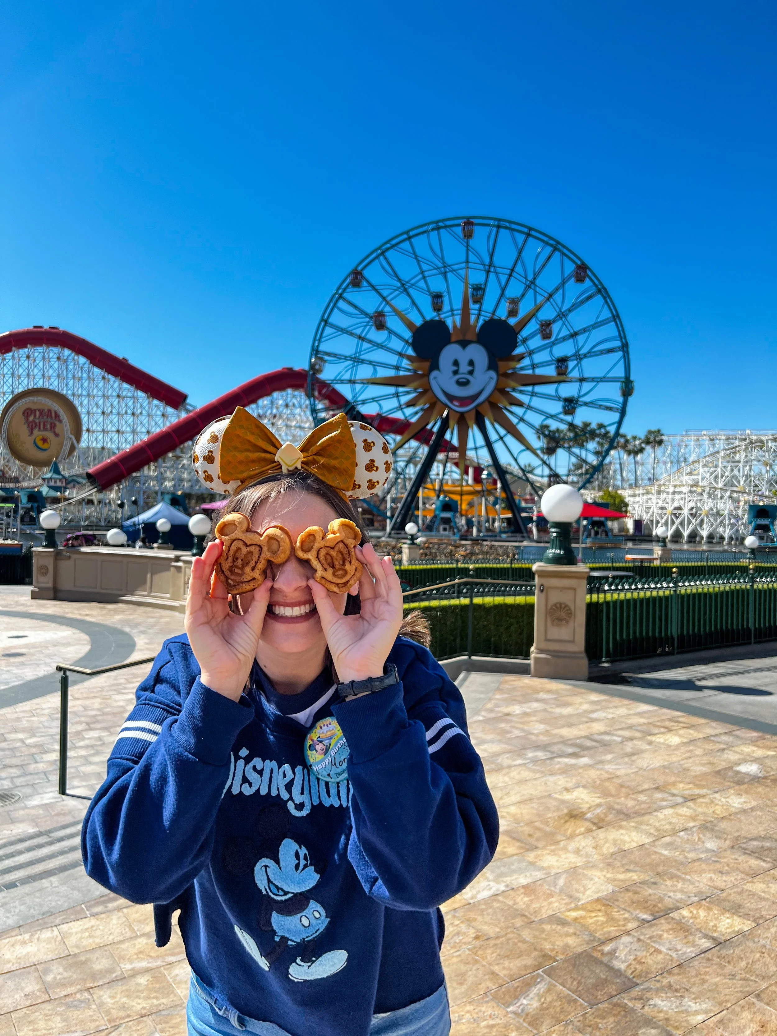 a woman holding mickey waffles in front of her eyes while staring in front of a carousel