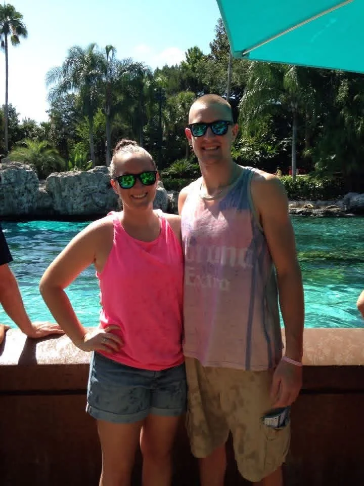 A couple smiles at the dolphin habitat railing at SeaWorld Orlando, turquoise water and palm trees behind them