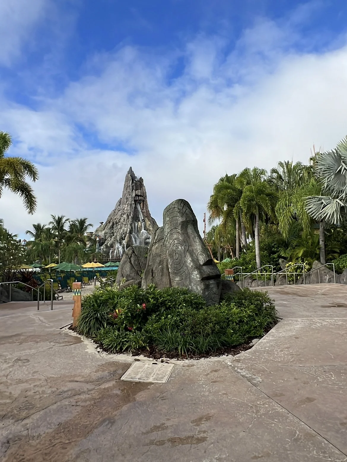 The Krakatau volcano centerpiece at Universal's Volcano Bay water park, surrounded by palm trees and a carved tiki rock statue.