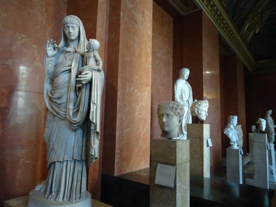 Classical marble statues and busts on display inside the Louvre Museum.