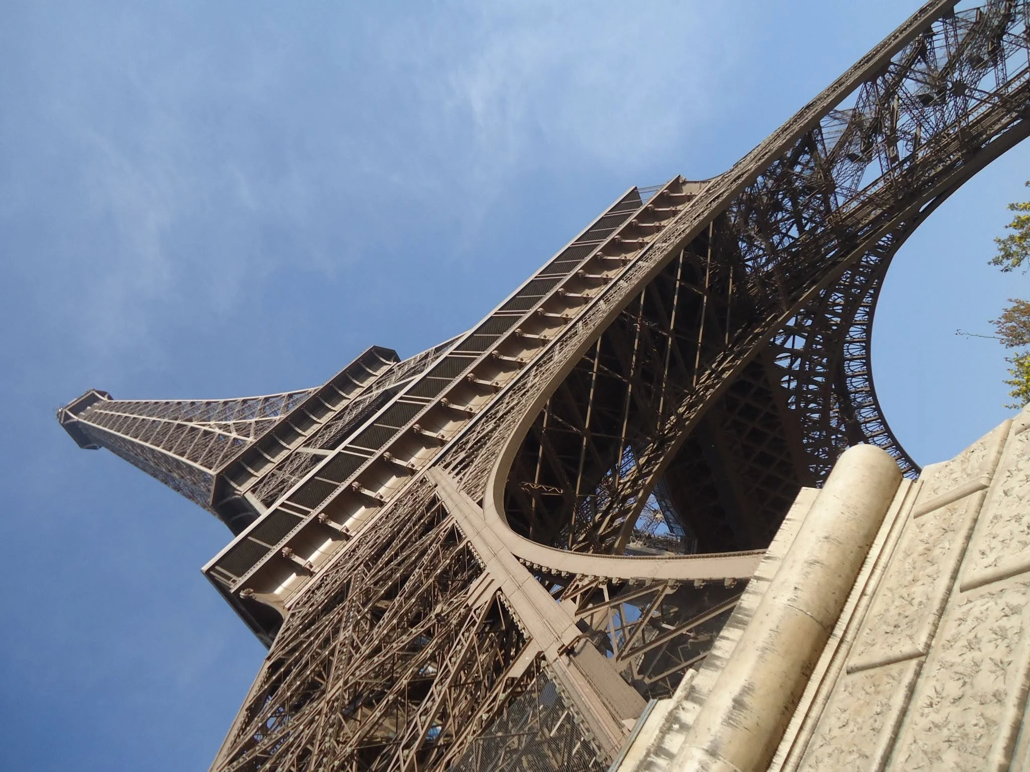 A dramatic upward view of the Eiffel Tower's iron latticework against a clear blue sky.