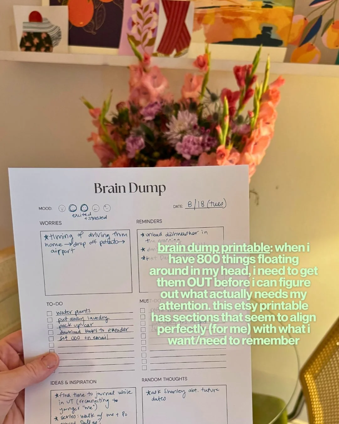 Hand holding a filled-out brain dump printable in front of a vase of pink flowers