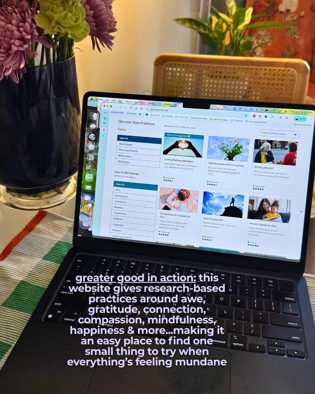 Laptop open to the Greater Good in Action website next to a vase of flowers