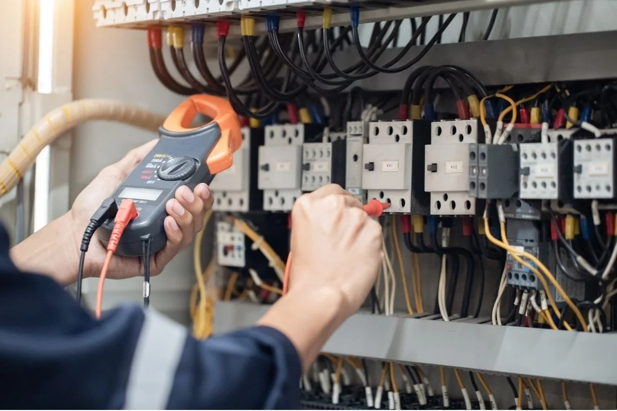 Person testing electrical circuit breaker panel with a multimeter.