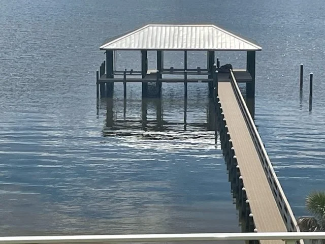 A wooden dock with a covered gazebo extending over a calm body of water.