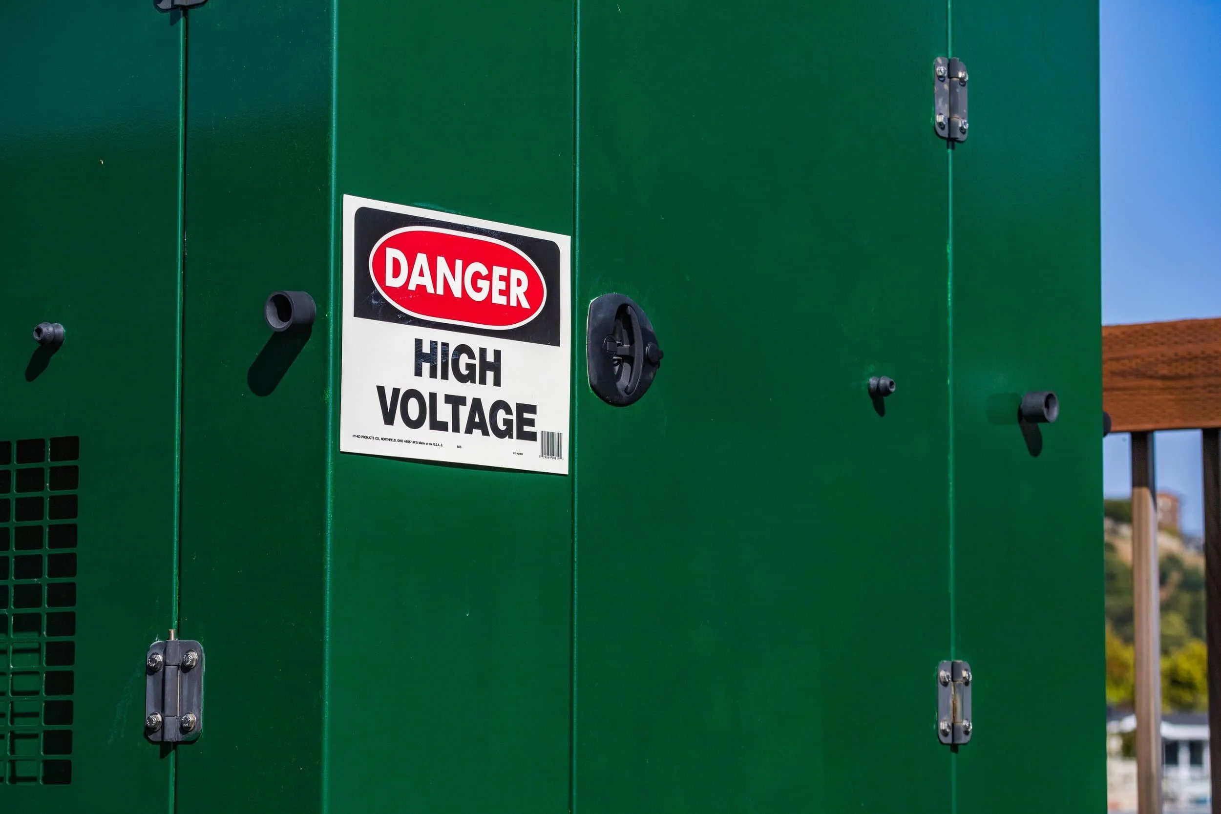 Green electrical box with a black and white warning sticker that reads 'Danger High Voltage'.