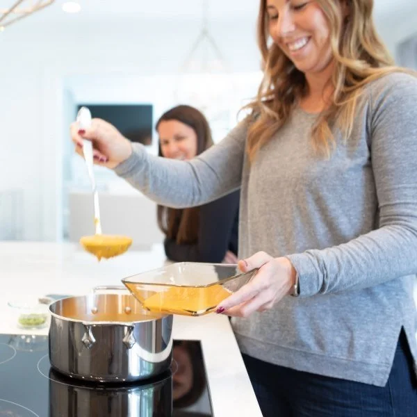 A woman standing in the kitchen with a ladle as she dishes up warm butternut squash soup.