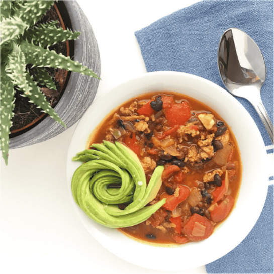 A bowl of warm chili with avocado chunks on top.
