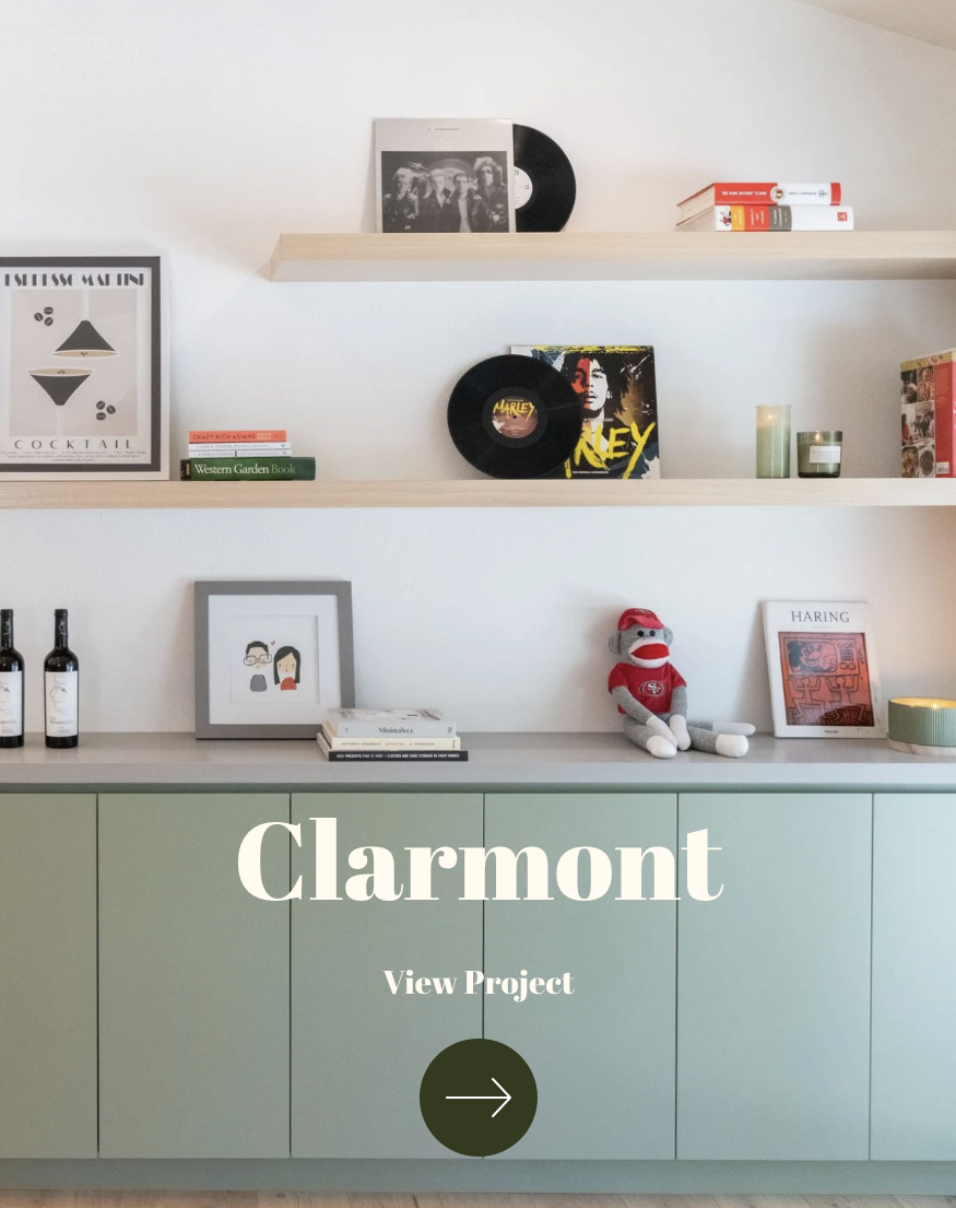 Interior view of a room with three white floating shelves displaying vinyl records, books, framed art, and decor. Below is a green cabinet with additional decorative items, including a plush toy, bottles, and framed artwork.