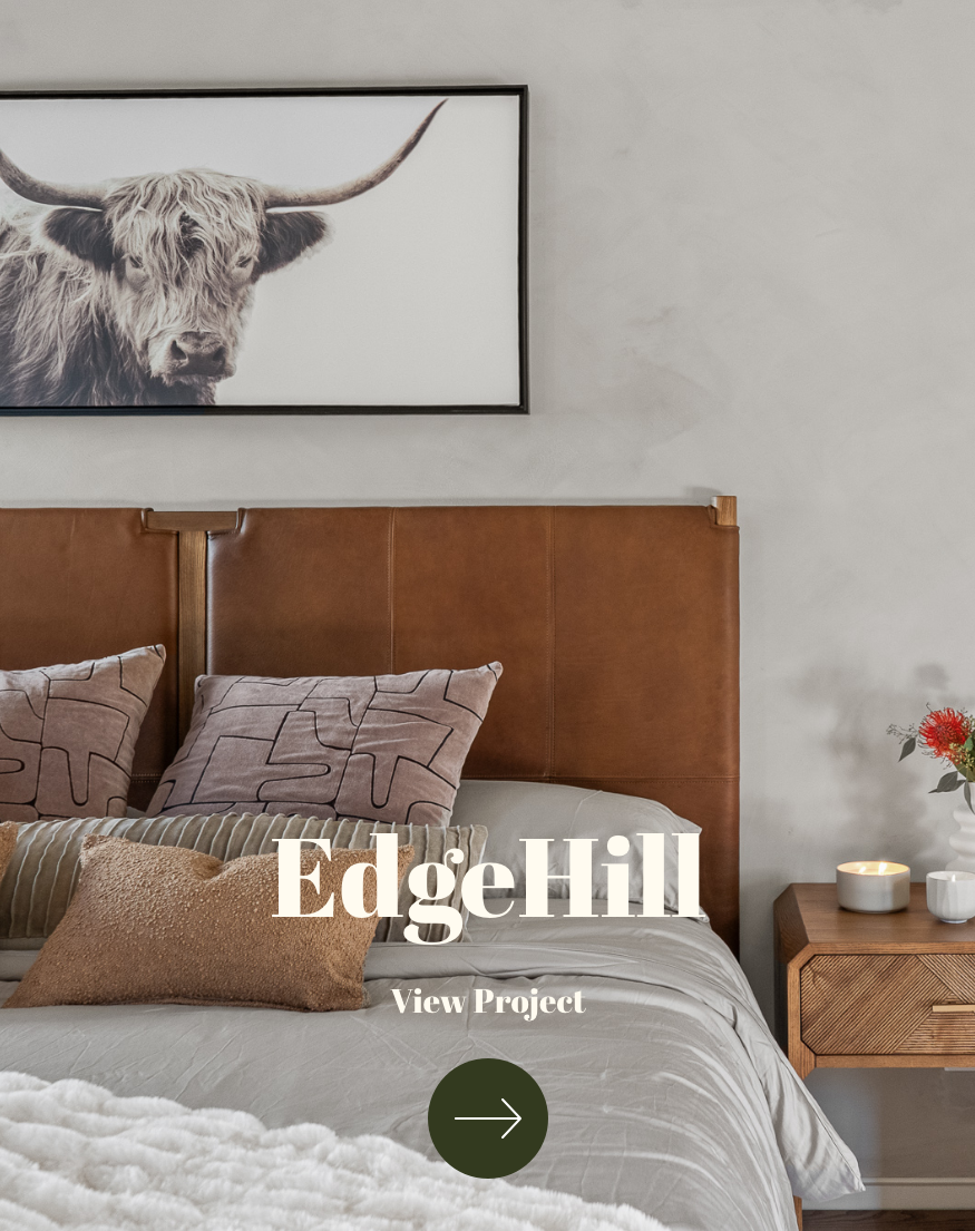 Interior bedroom with a large framed black and white photo of a Highland cow on the wall above a brown leather headboard. The bed has multiple pillows and a beige throw. To the side, there's a wooden nightstand with a white flower vase, a lit candle, and small containers. The text over the image reads "EdgeHill View Project" with a green arrow button below.
