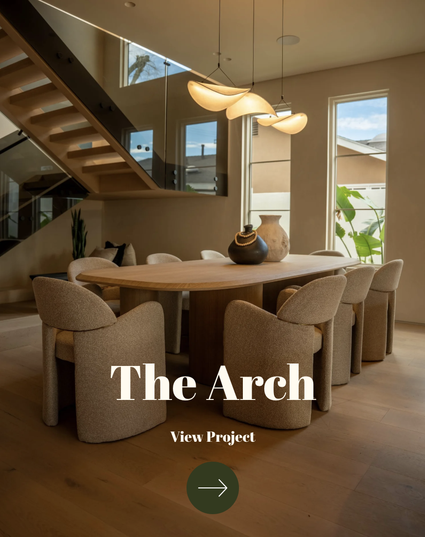 Modern dining room with a large wooden table surrounded by eight upholstered beige chairs, decorative vases on the table, and contemporary pendant lighting, with tall windows showing an outdoor view.
