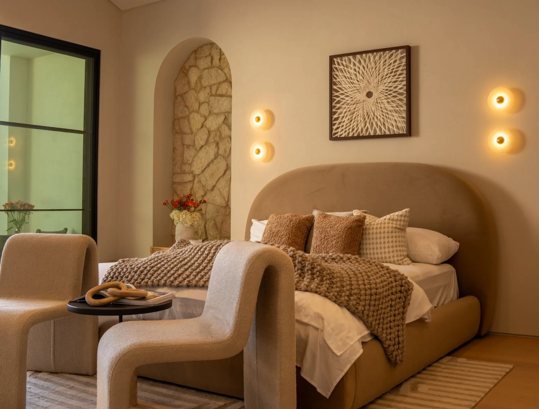 Modern living room with white curved sofa, wooden coffee table, beige rug, and open kitchen with bar stools and floating shelves.