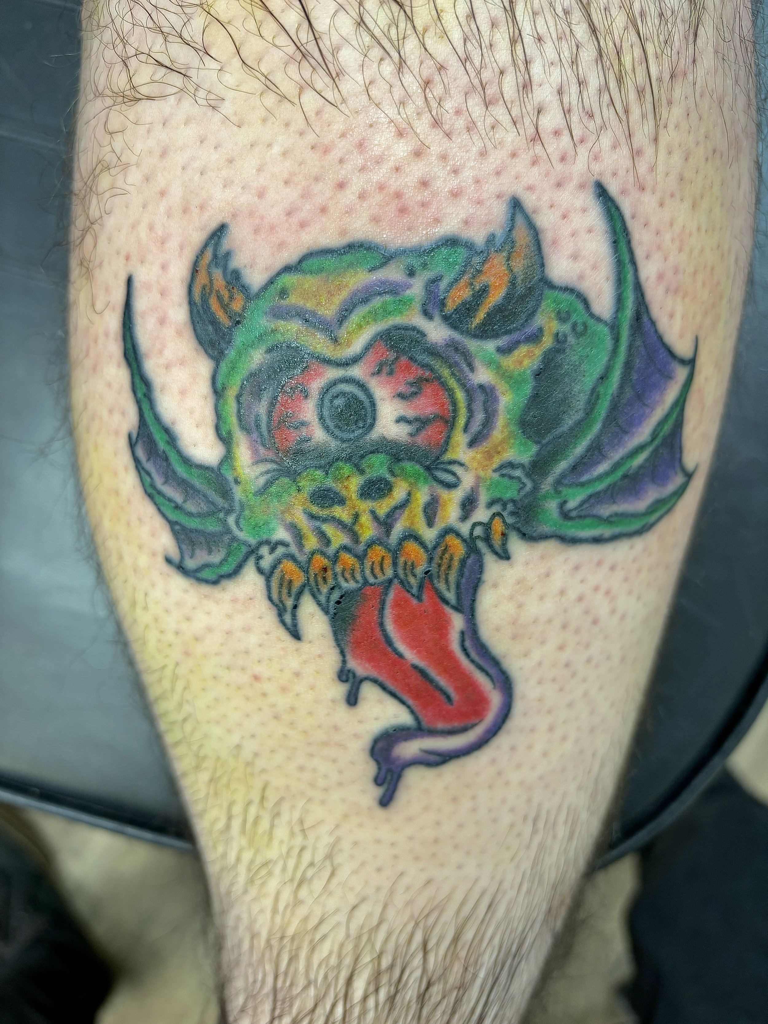 Colorful monster tattoo with one eye, sharp teeth, horns, and wings on skin.