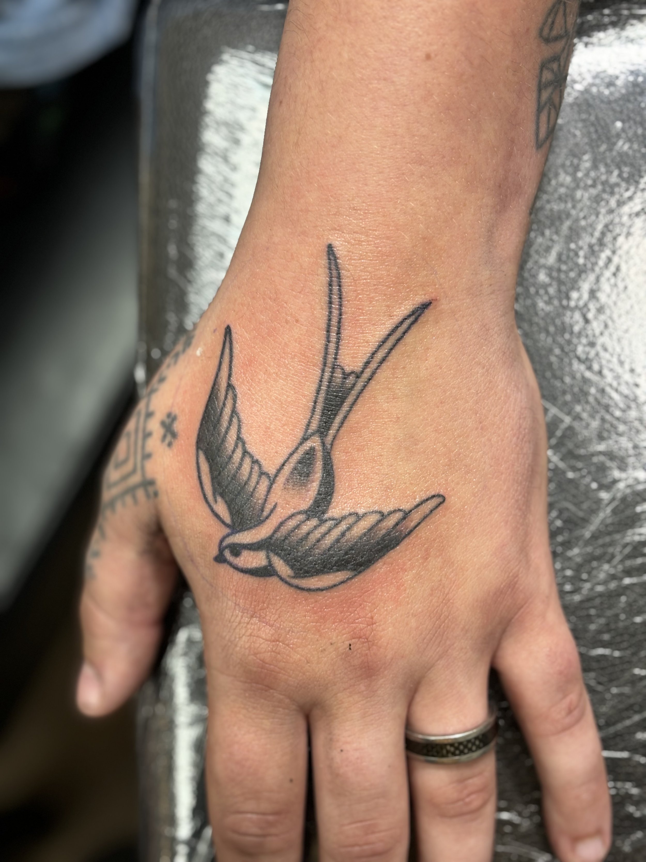 Hand tattoo of a bird in flight on the back of a hand.