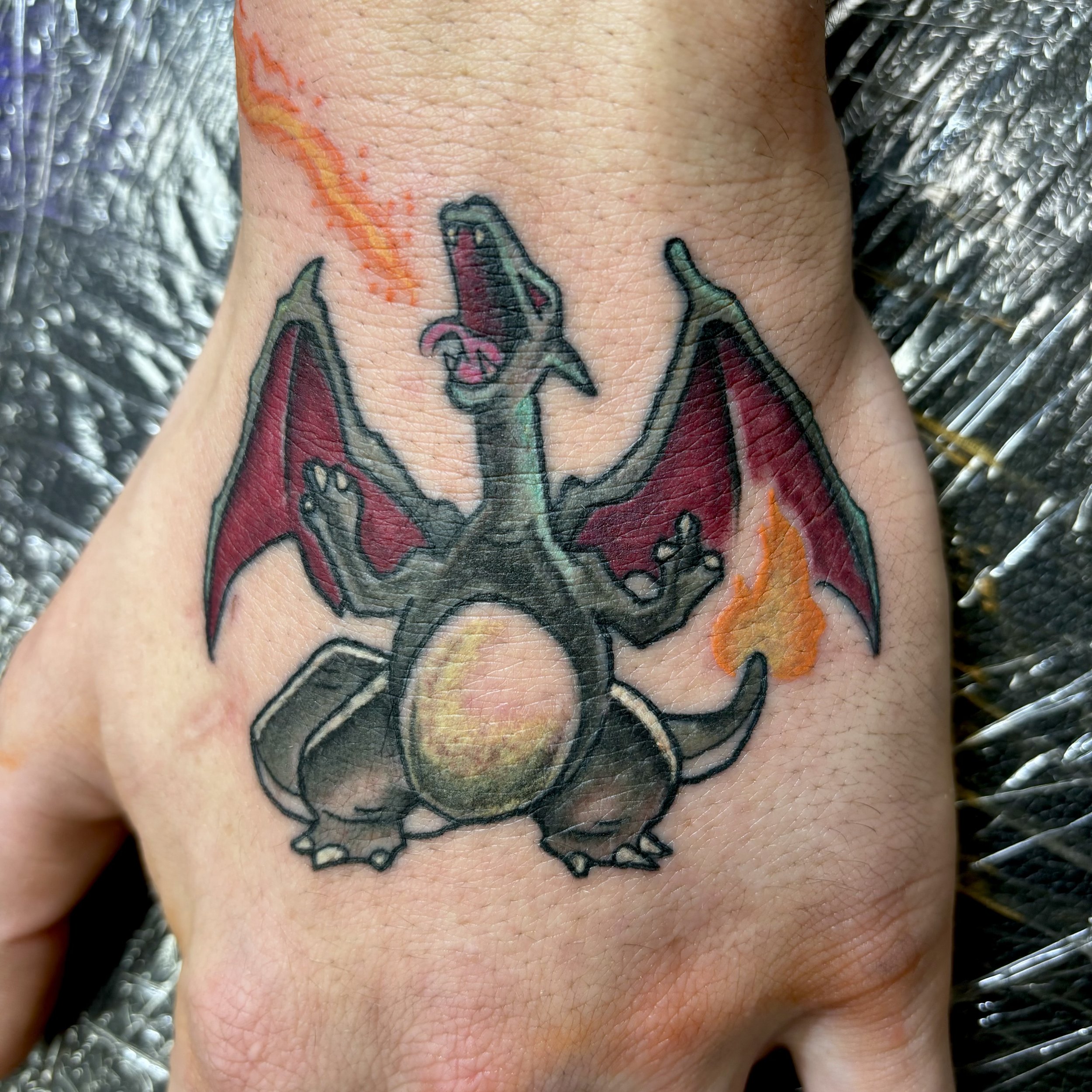 Hand tattoo of a dragon with wings and flames.