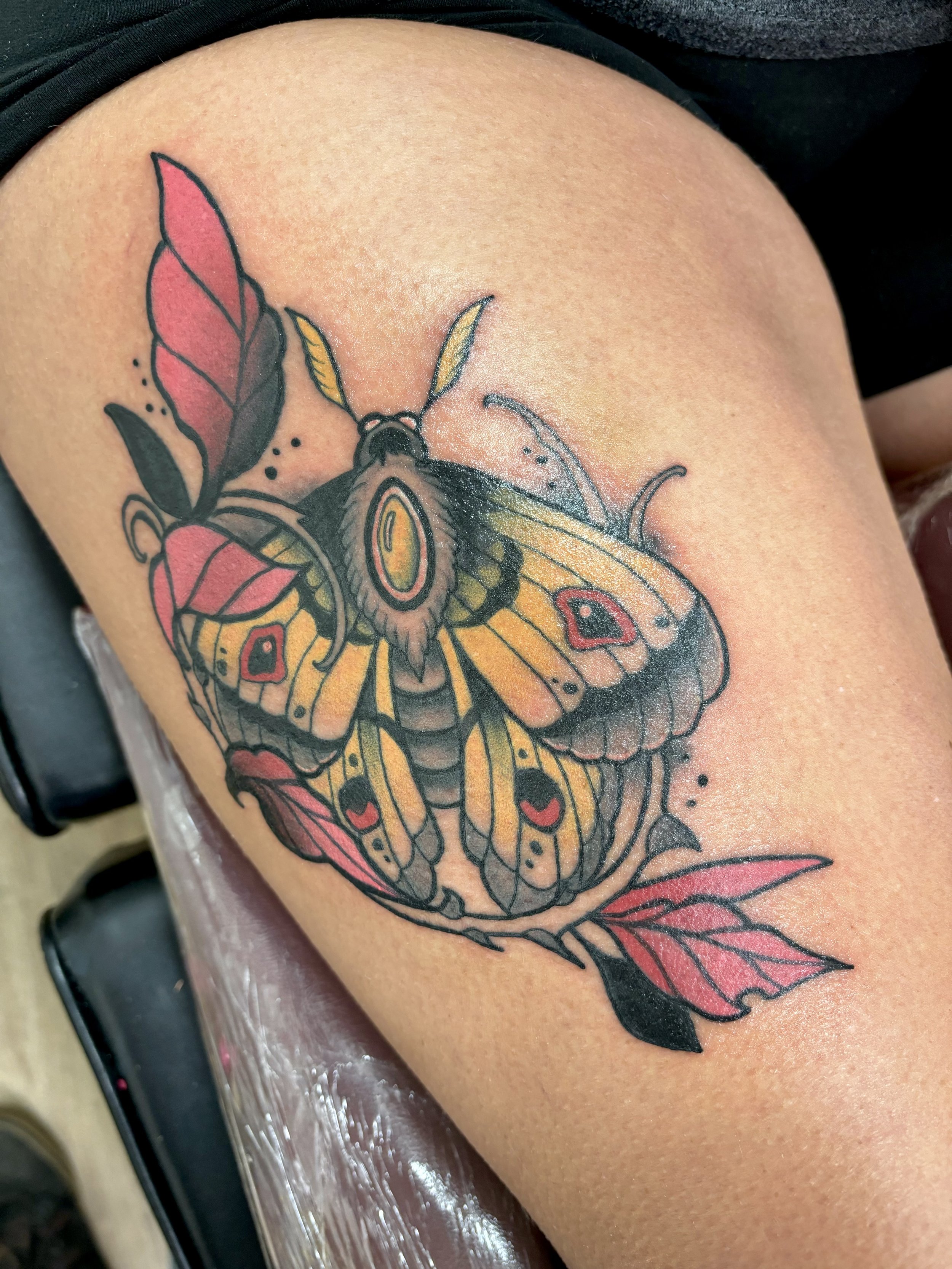 Tattoo of a colorful moth with pink leaves on skin
