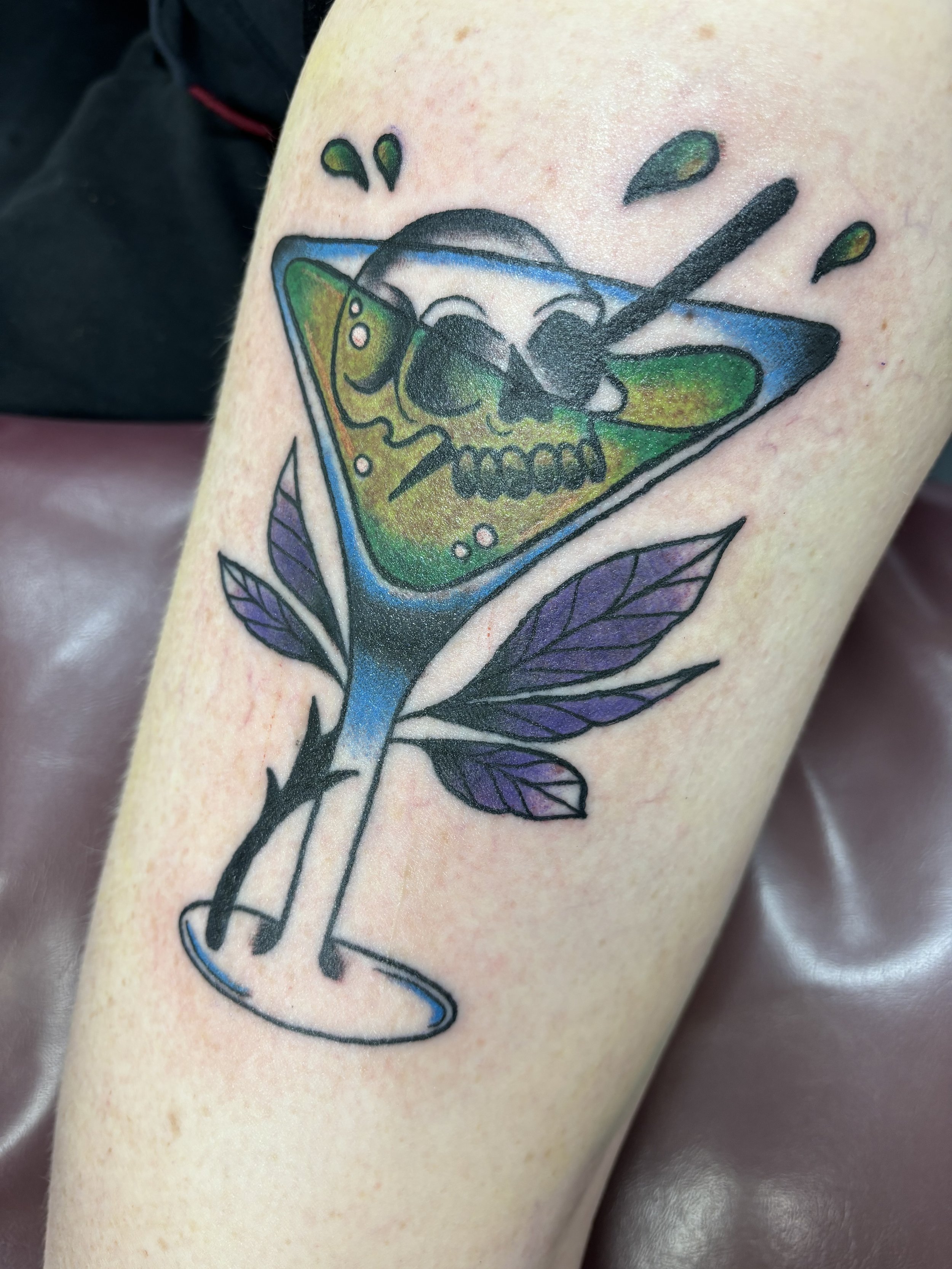 Tattoo of a colorful cocktail glass with a skull and leaves design