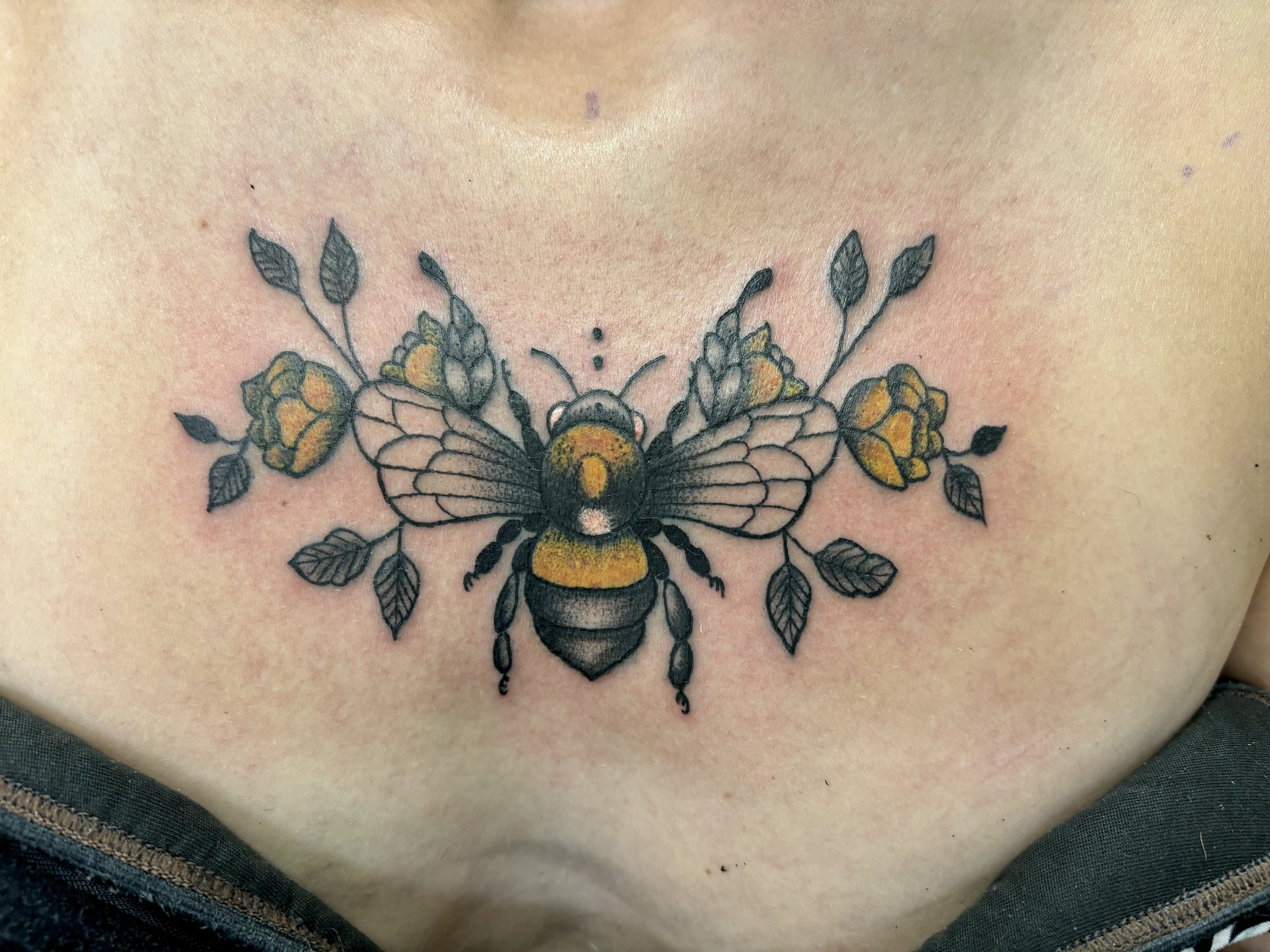Tattoo of a bee with yellow flowers and leaves on chest