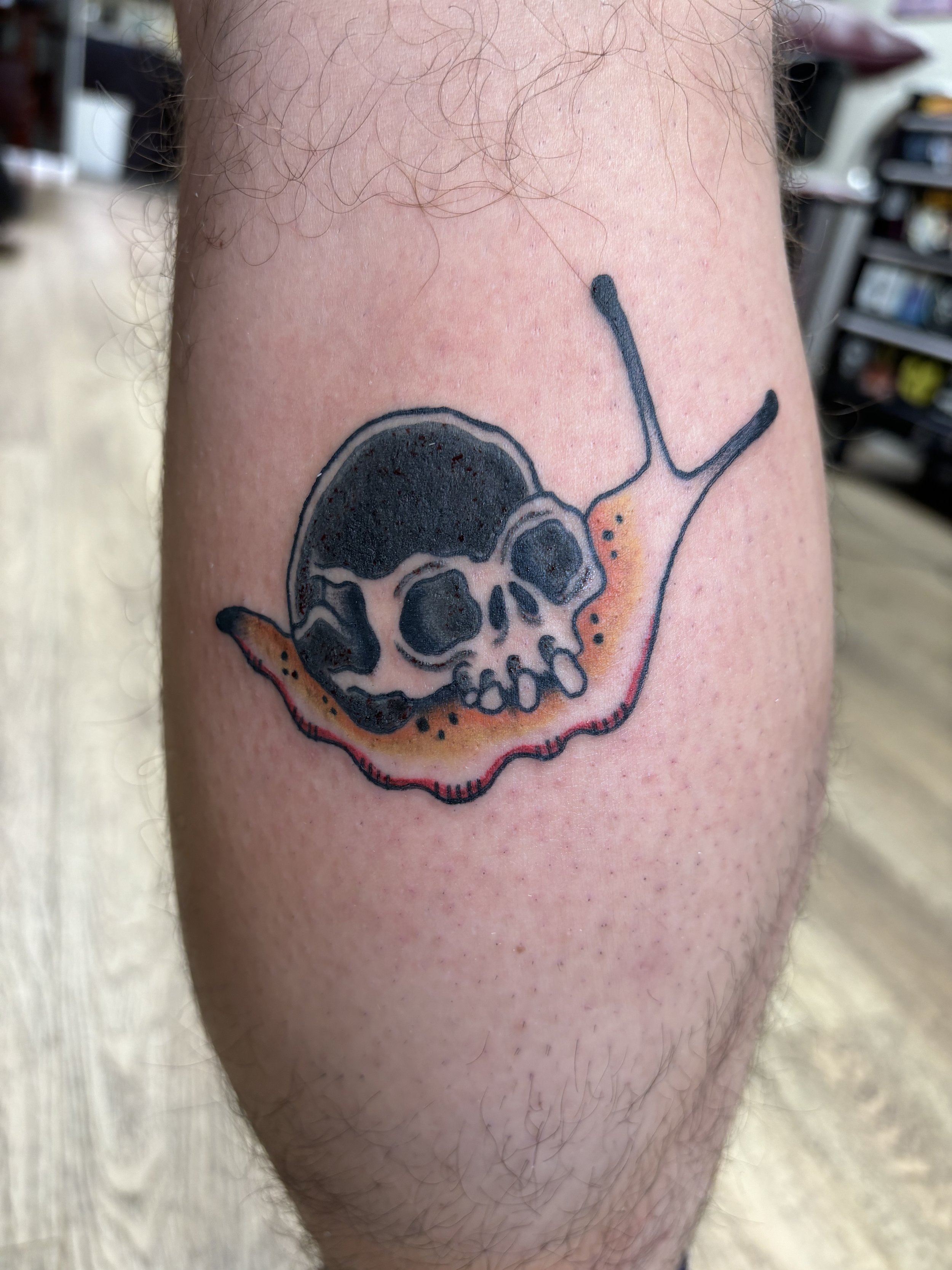 Tattoo of a snail with a skull on its back on a person's calf.