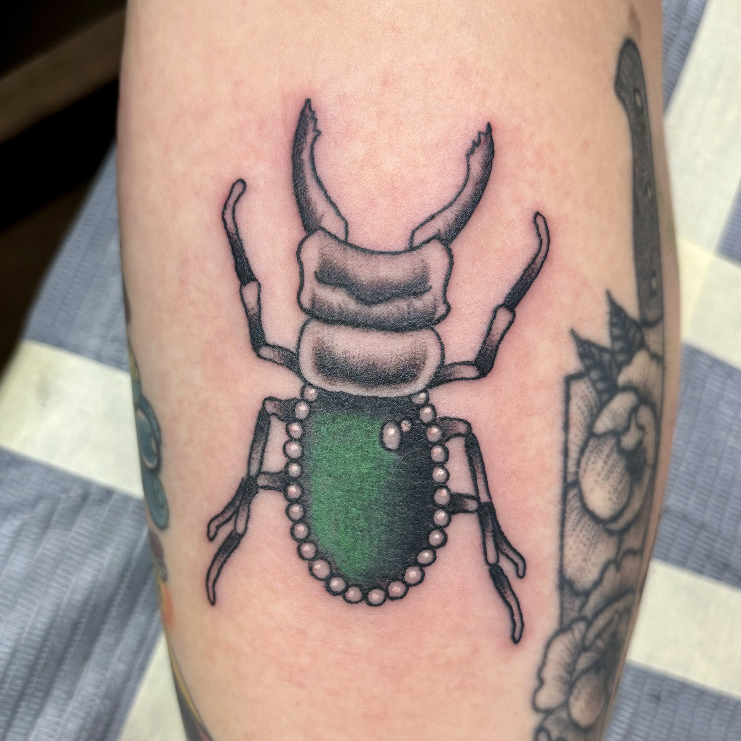 Tattoo of a beetle with a green shell and pearls on a person's skin.