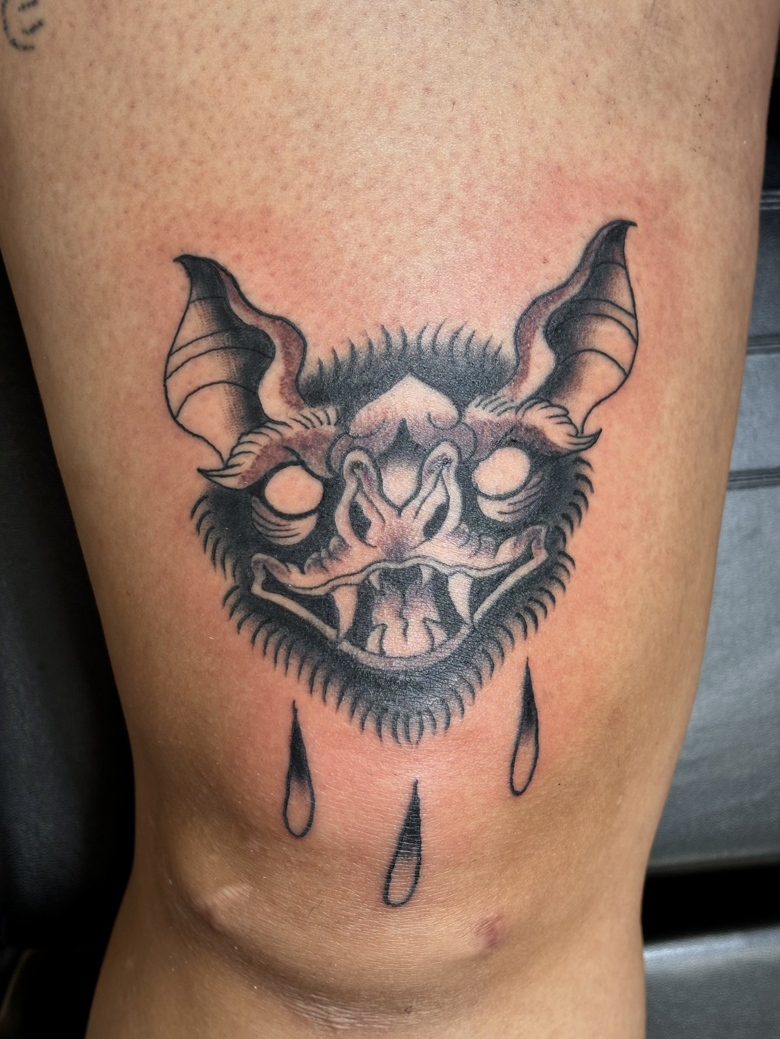 Tattoo of a horned demon face with tears, black ink design, on skin.