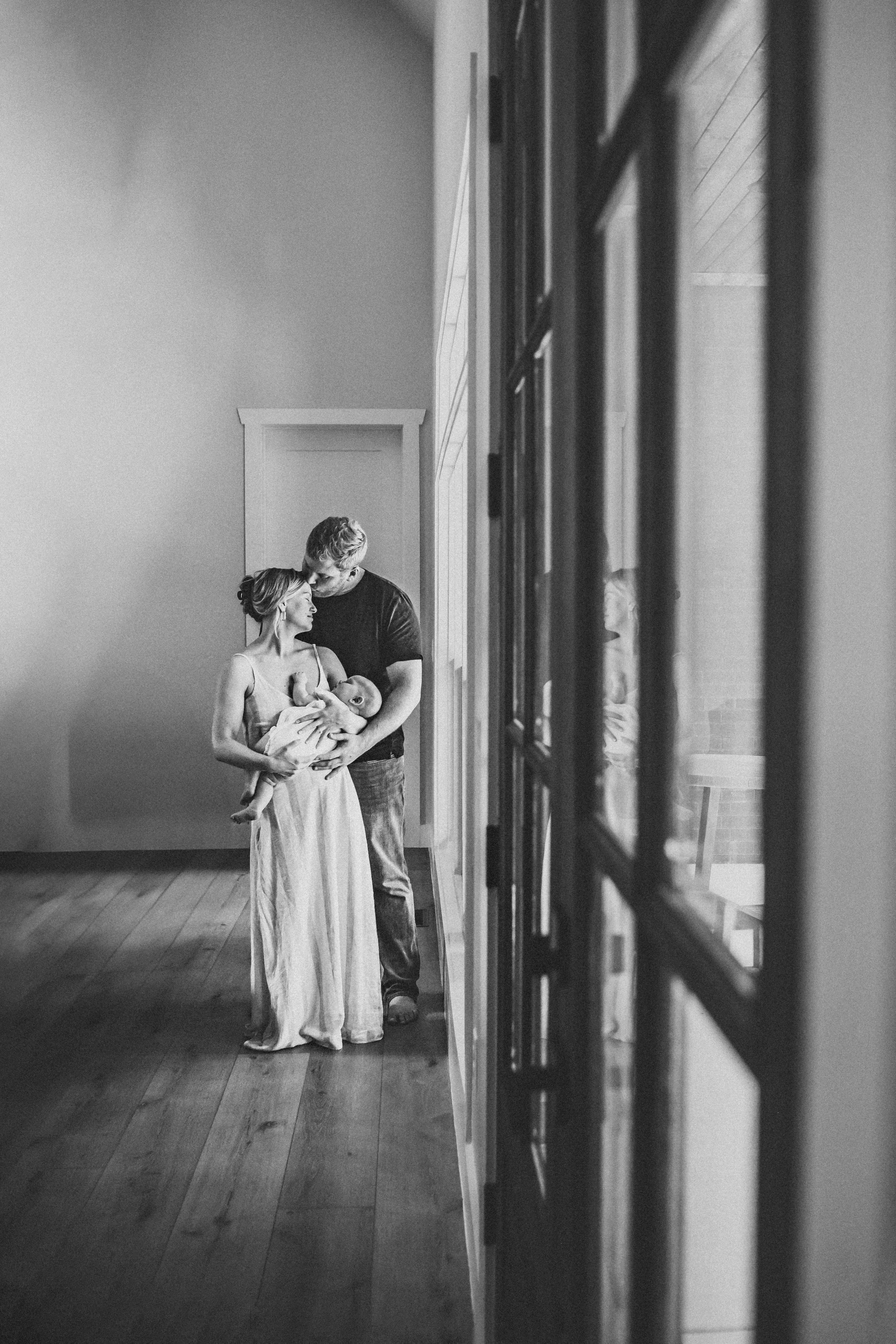 Lifestyle 6 month Milestone photography session. Mother and father kissing and holding their sleeping baby.