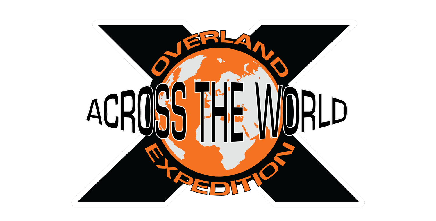 Logo for the Overland Across the World Expedition featuring an orange globe with white continents, crossed by white and black lines, and the words "OVERLAND" at the top, "ACROSS THE WORLD" in the middle, and "EXPEDITION" at the bottom.