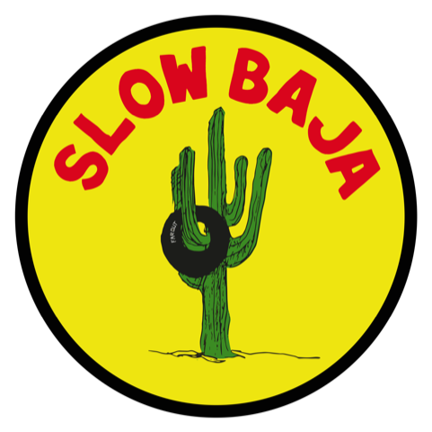 A yellow circular logo with a black border featuring the words 'SLOW BAJA' in red, and an illustration of a green cactus with a black tire around its middle.