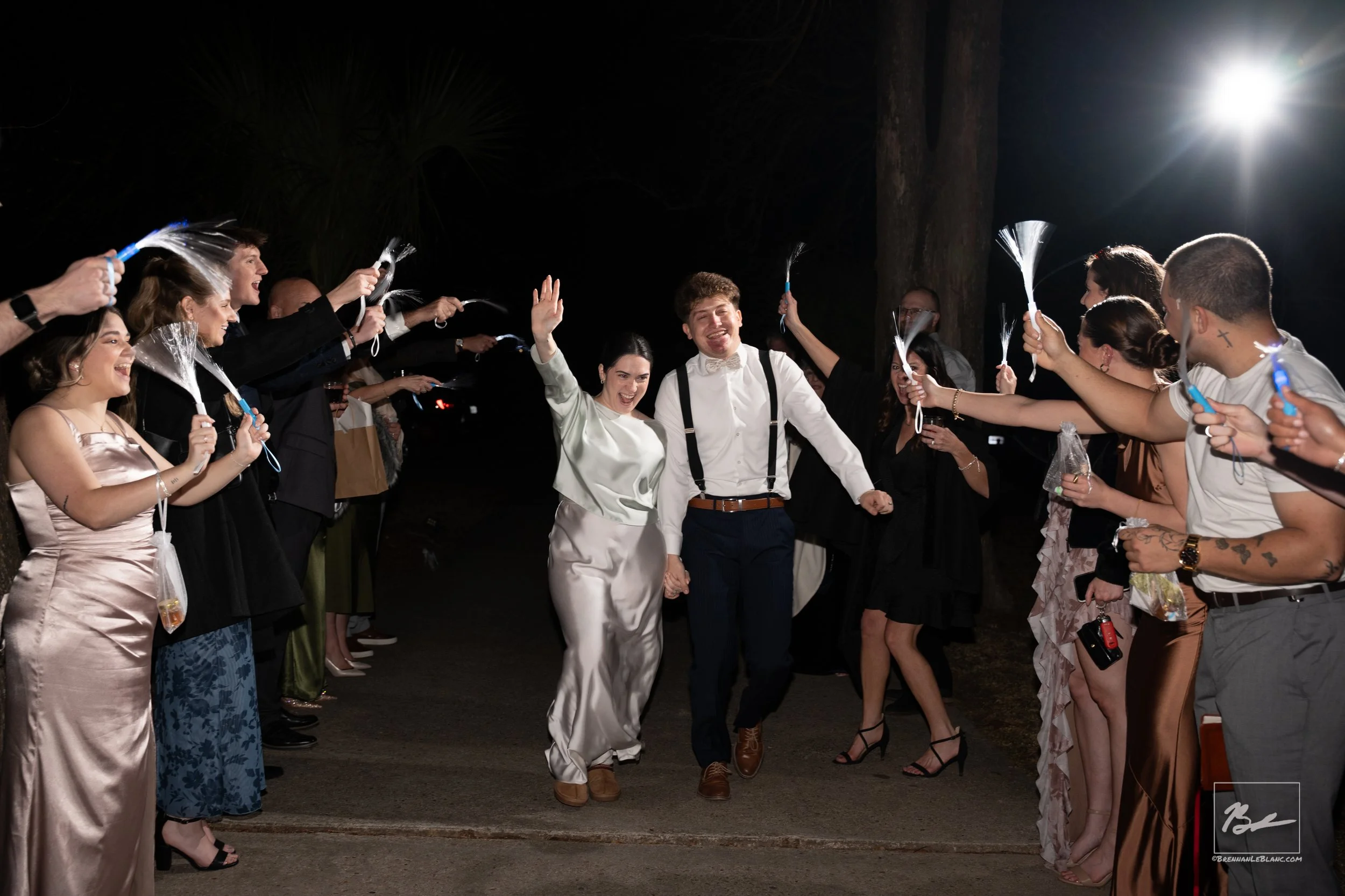 A wedding celebration with the bride and groom walking through a line of guests holding sparklers at night.