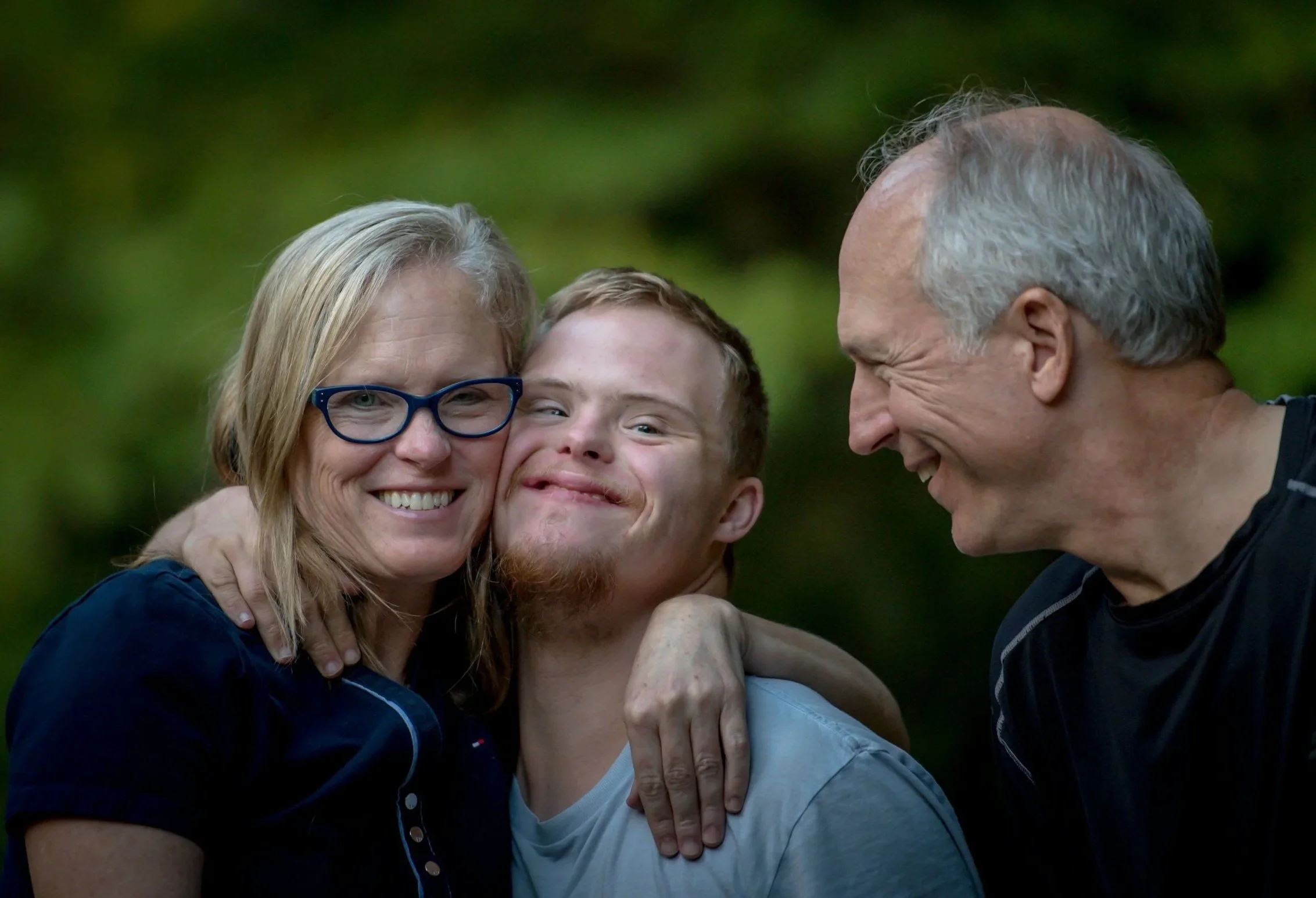 A family of three smiling and hugging outdoors with a green background in Bathurst NSW