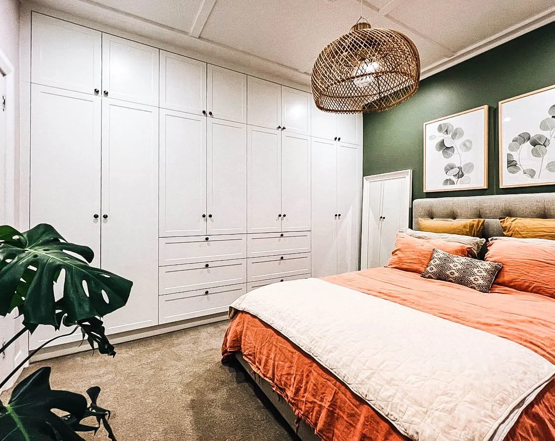 White panel door wardrobe in bedroom with green walls, a salmon bedspread and monstera plant
