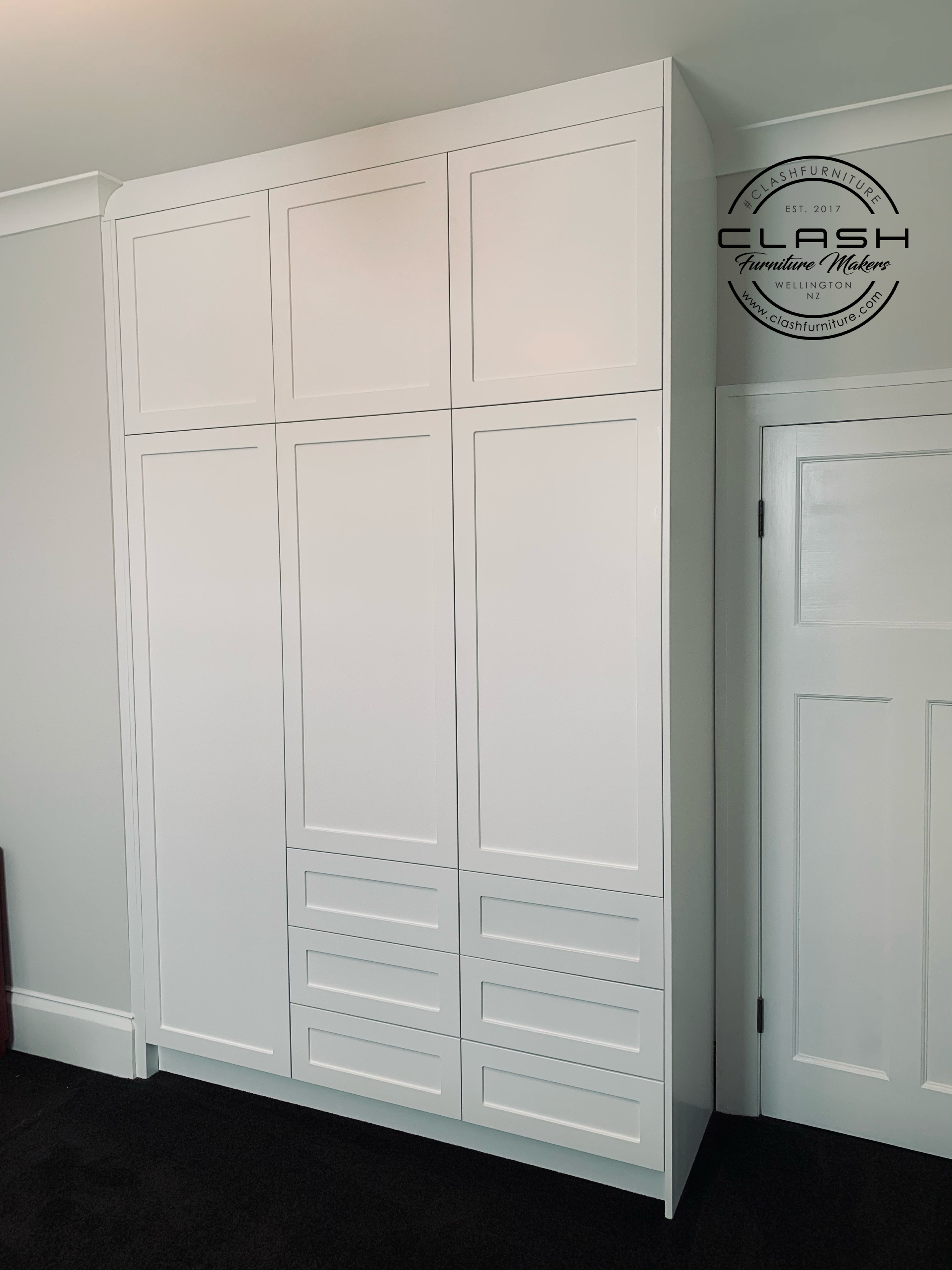 Built in white panel wardrobe in bedroom with light grey walls and white door