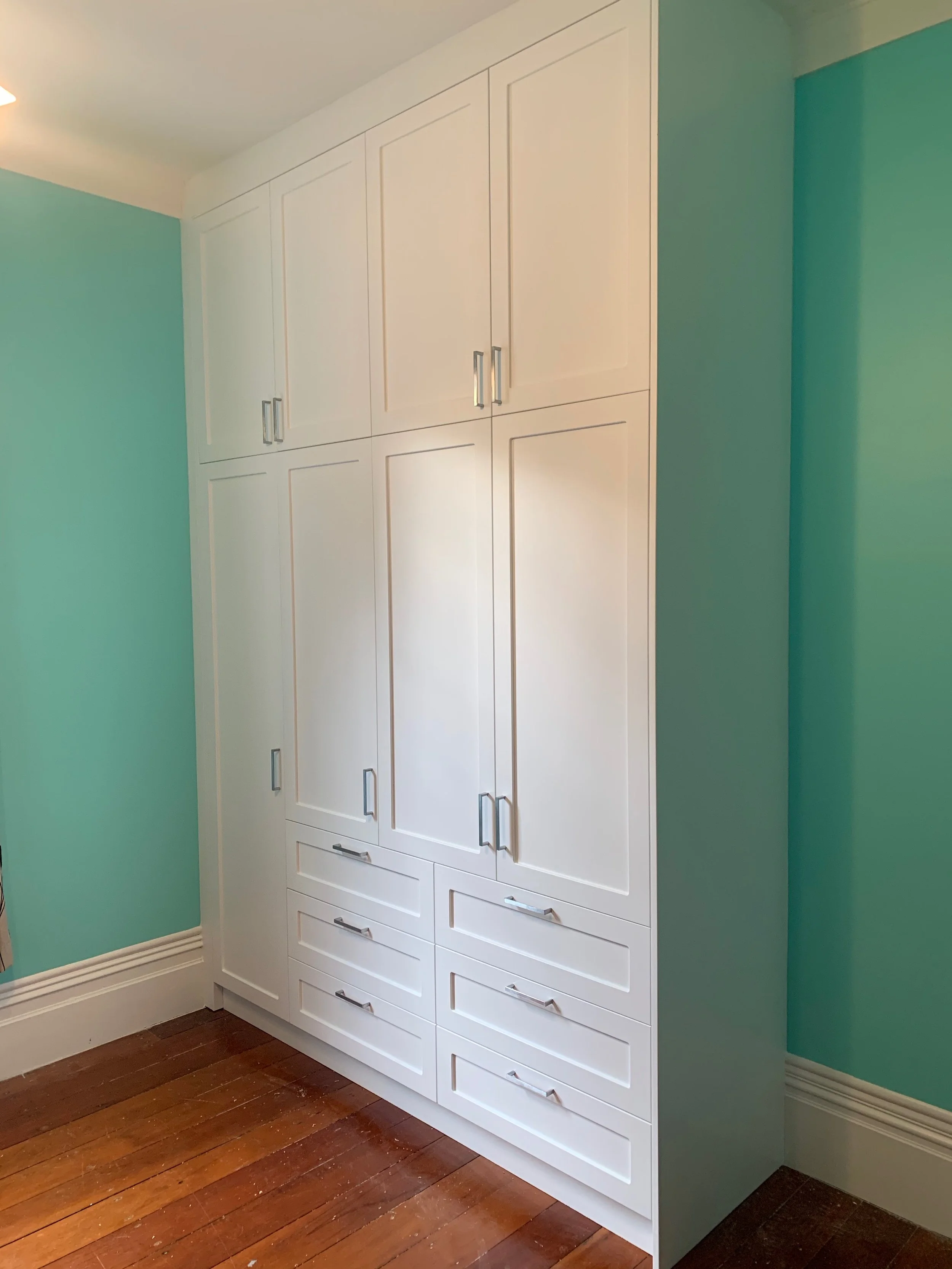 White panel wardrobe with chrome handles in room with aqua walls