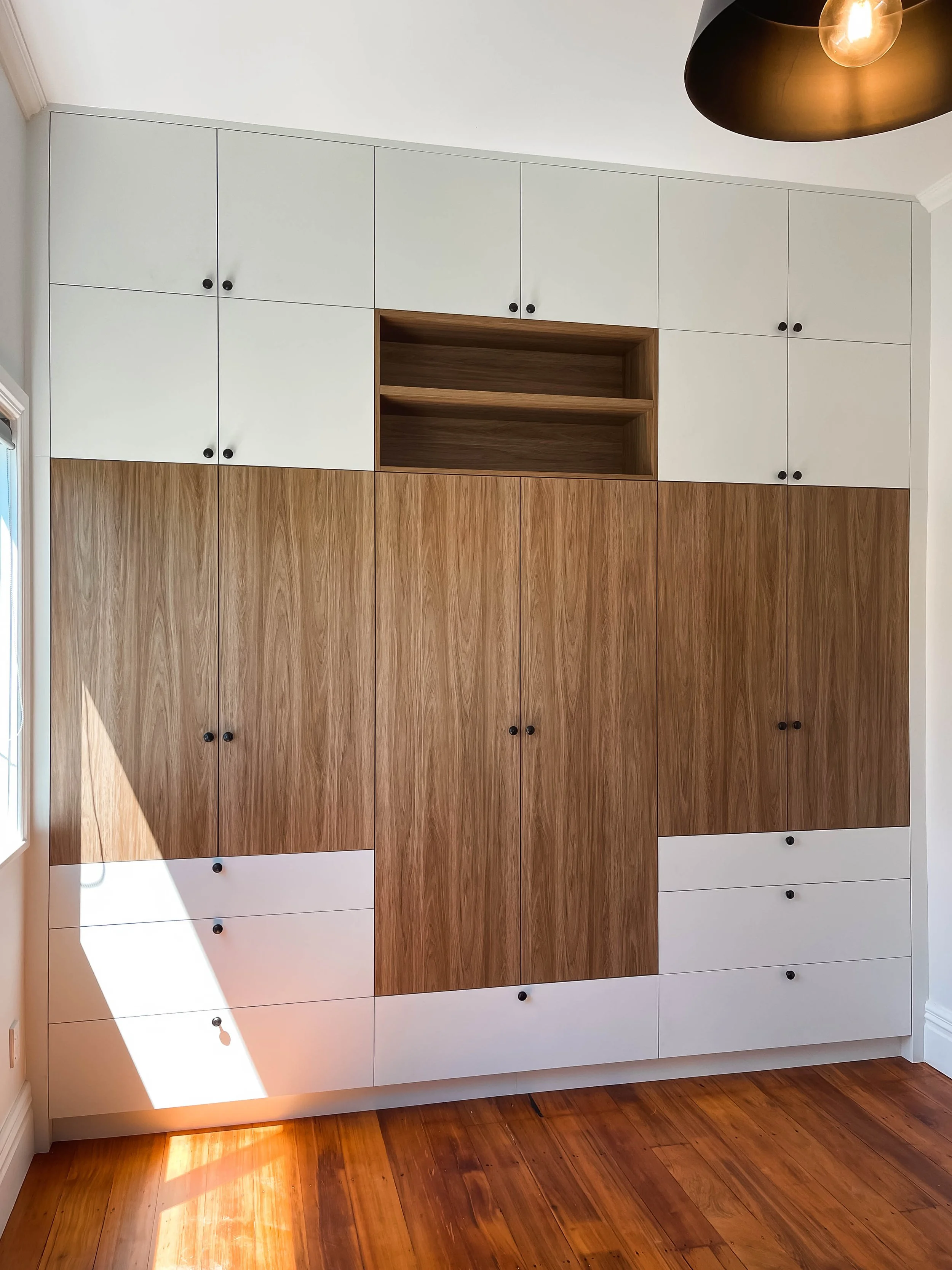 White and timber look melteca flat door wardrobe with black handles in room with wooden floors