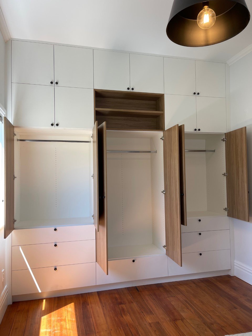 Open view of White and timber look melteca flat door wardrobe with black handles, clothes hanging spaces seen inside