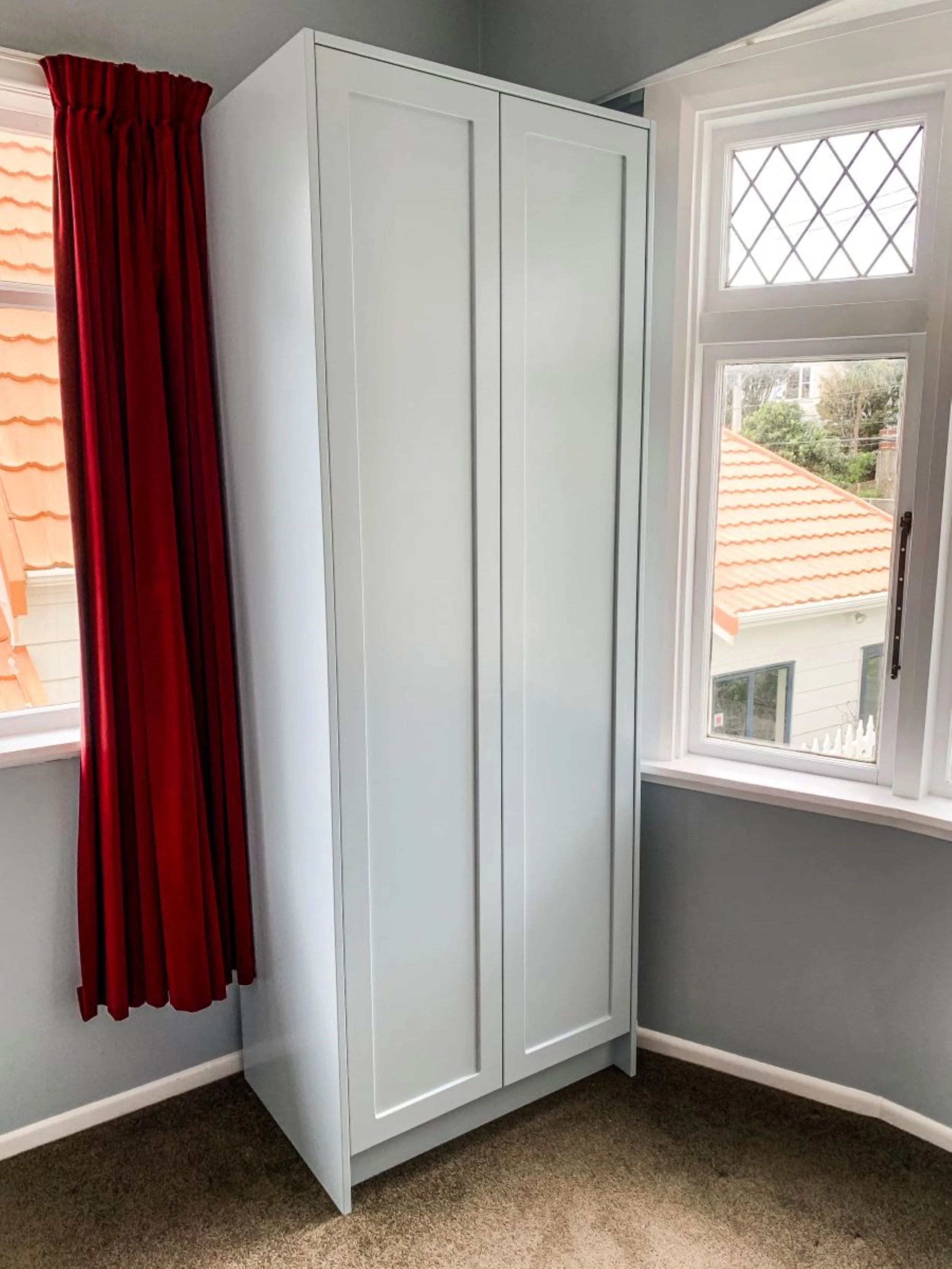 Free standing wardrobe with panel doors in room with red curtain