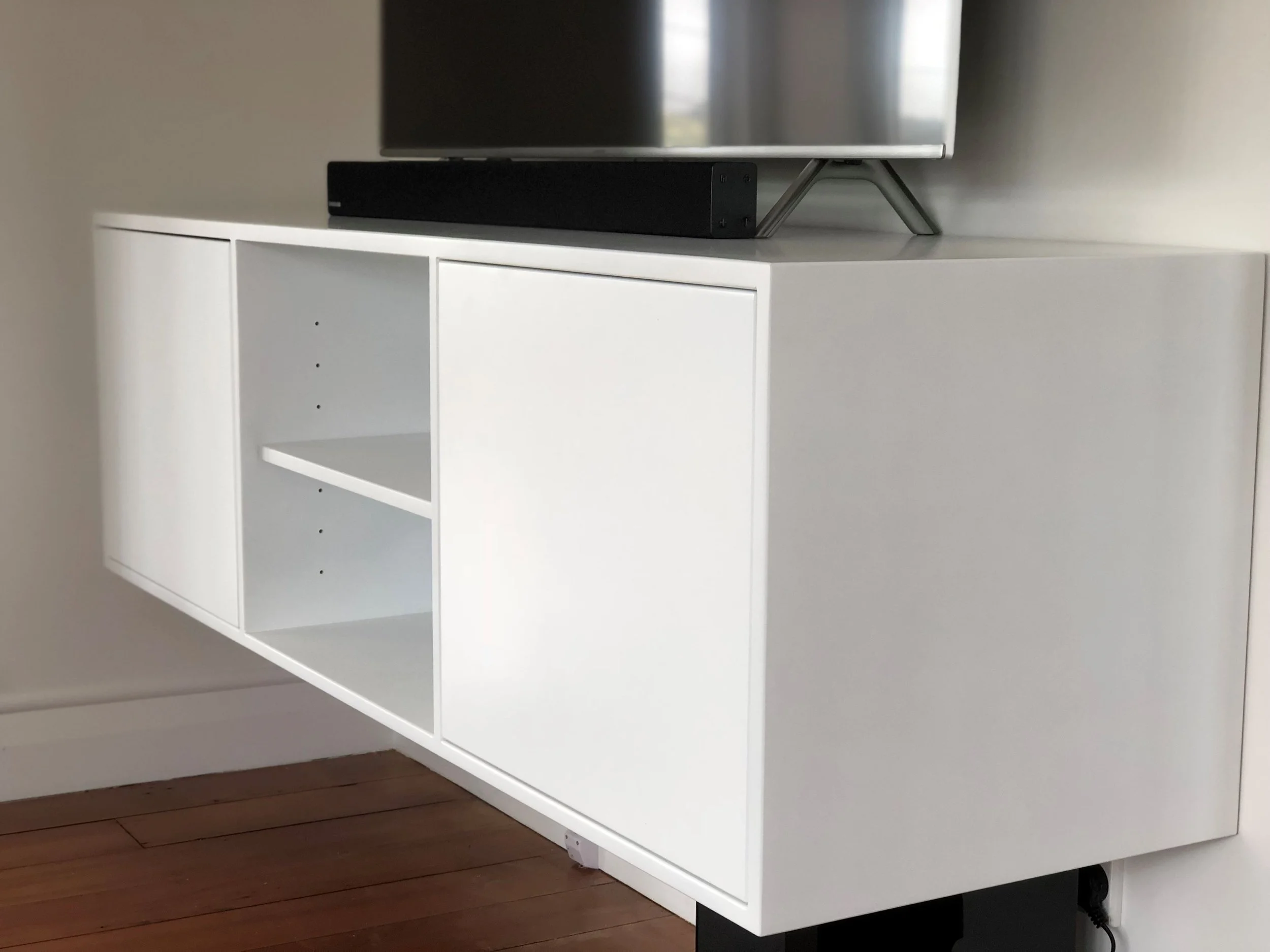 White melteca entertainment unit with cabinet at either end and shelves in the middle displaying a tv on top