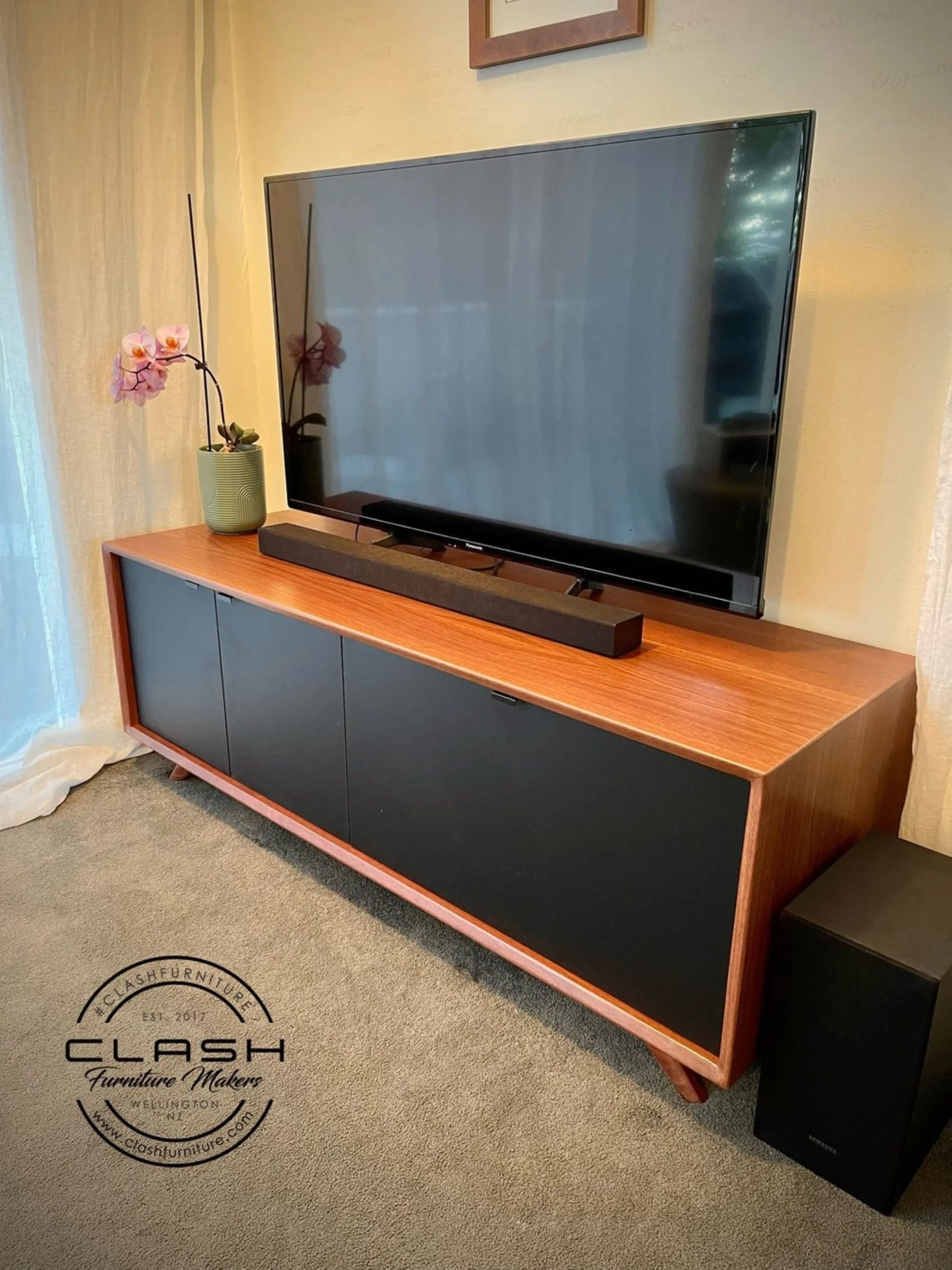 Jerrah entertainment unit with dark melteca doors, displaying tv on tp and green vase with pink orchid 