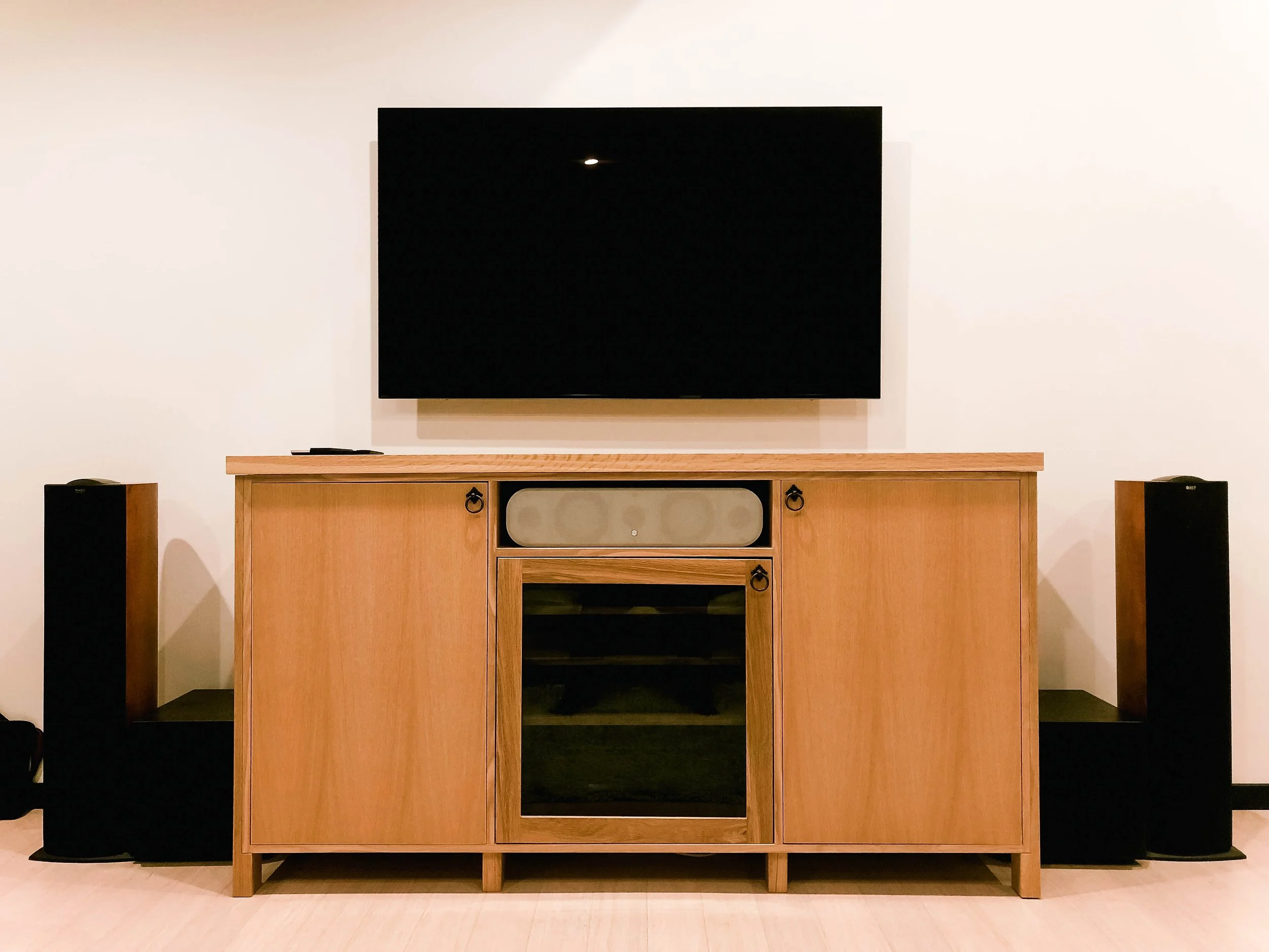 Wooden entertainment unit with black handles and a wall hung tv above 