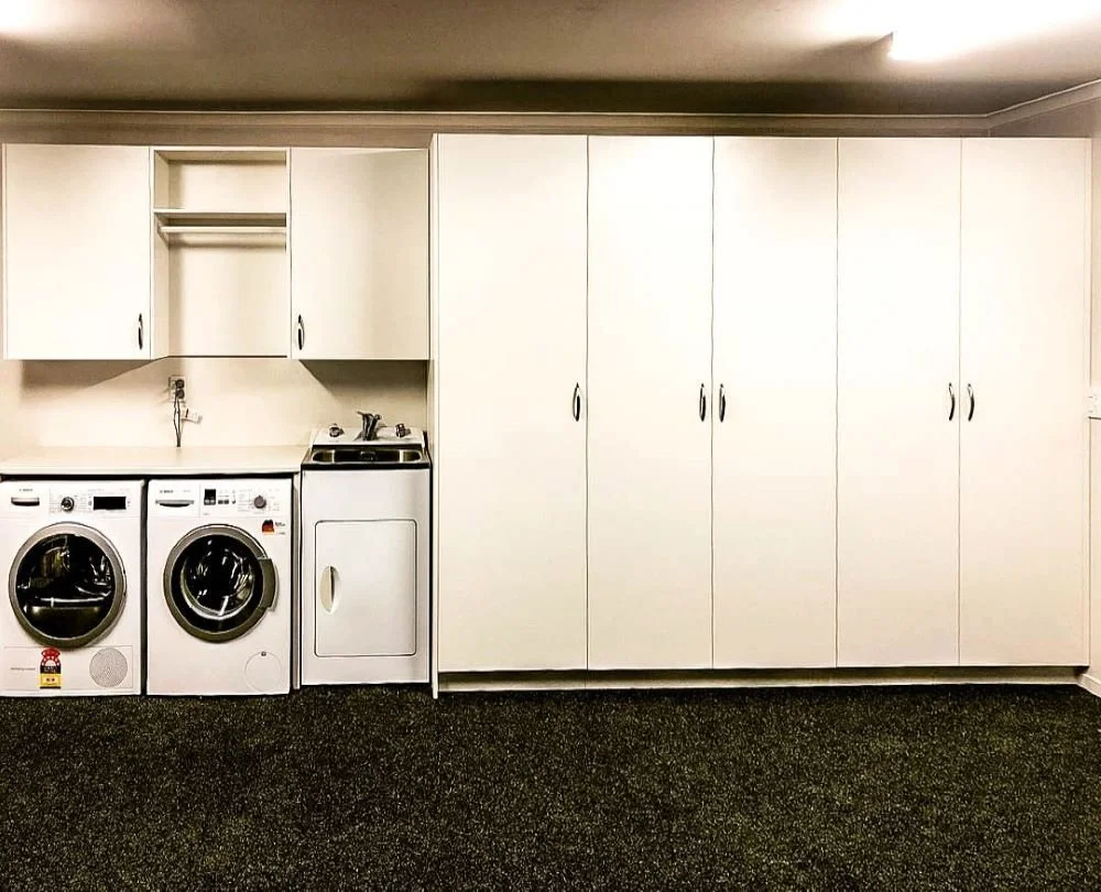White melteca tall and wall hung cabinets built around washing sink, washing machine and dryer which are visible