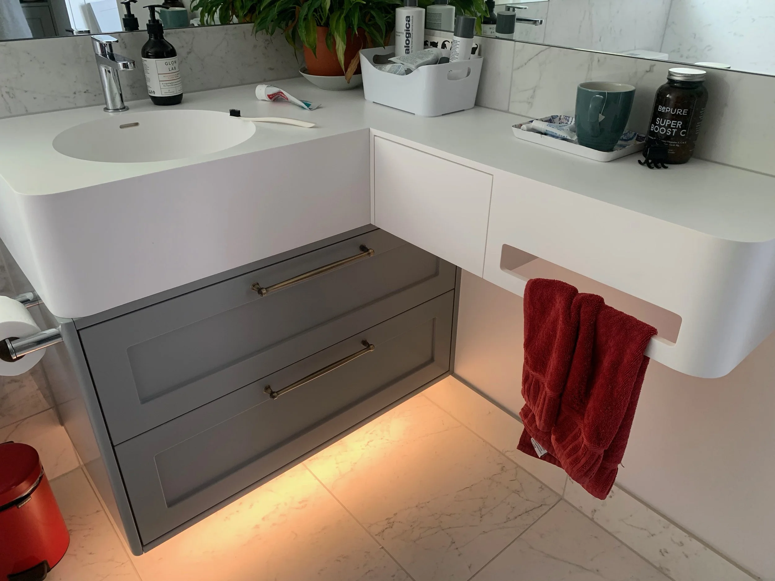 Grey bathroom vanity with white benchtop with built in basin. A red towel hangs on a built in towel rail. Bathroom items sit on bechtop