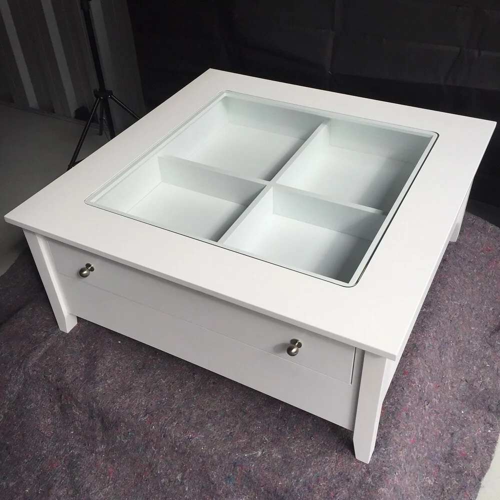 White coffee table with pull out drawer. the interior of the drawer is visible through the glass top cut put in the coffee table looking down into the drawer storage space
