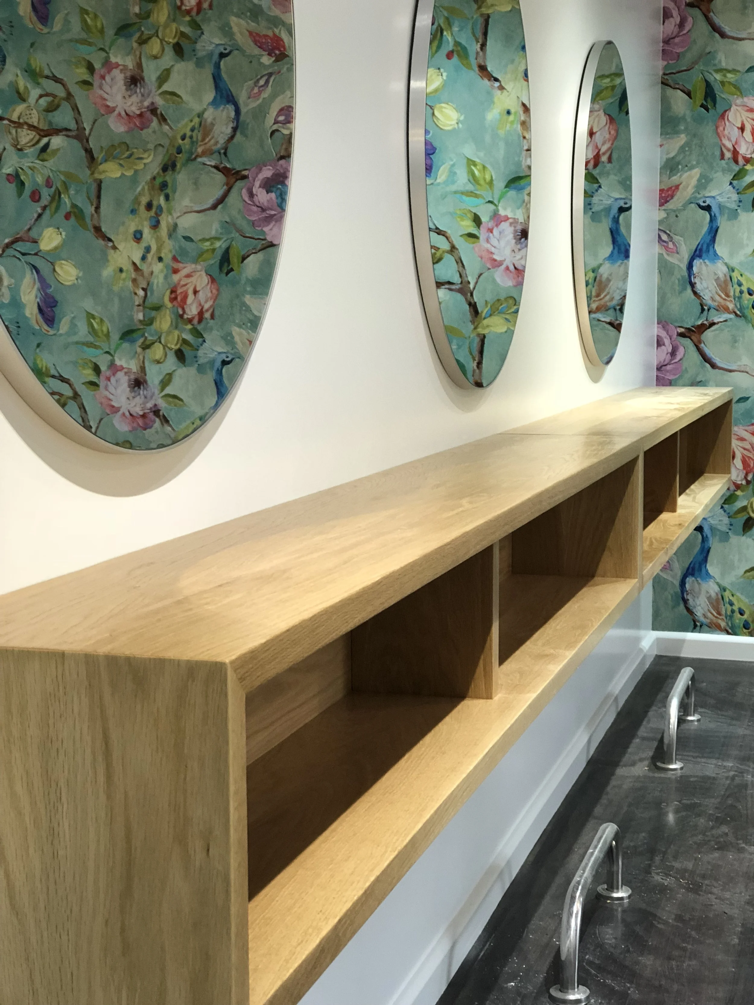 Wooden box shelving with wall hung mirrors reflecting colourful peacock wallpaper